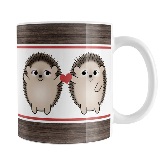 Cute Hedgehogs Holding Red Heart Mug (11oz) at Amy's Coffee Mugs. A ceramic coffee mug designed with cute and happy hedgehogs holding a red heart together between them, on both sides of the mug, over white with a rustic wood and red stripe on the top and the bottom in a design that wraps around the mug up to the handle.