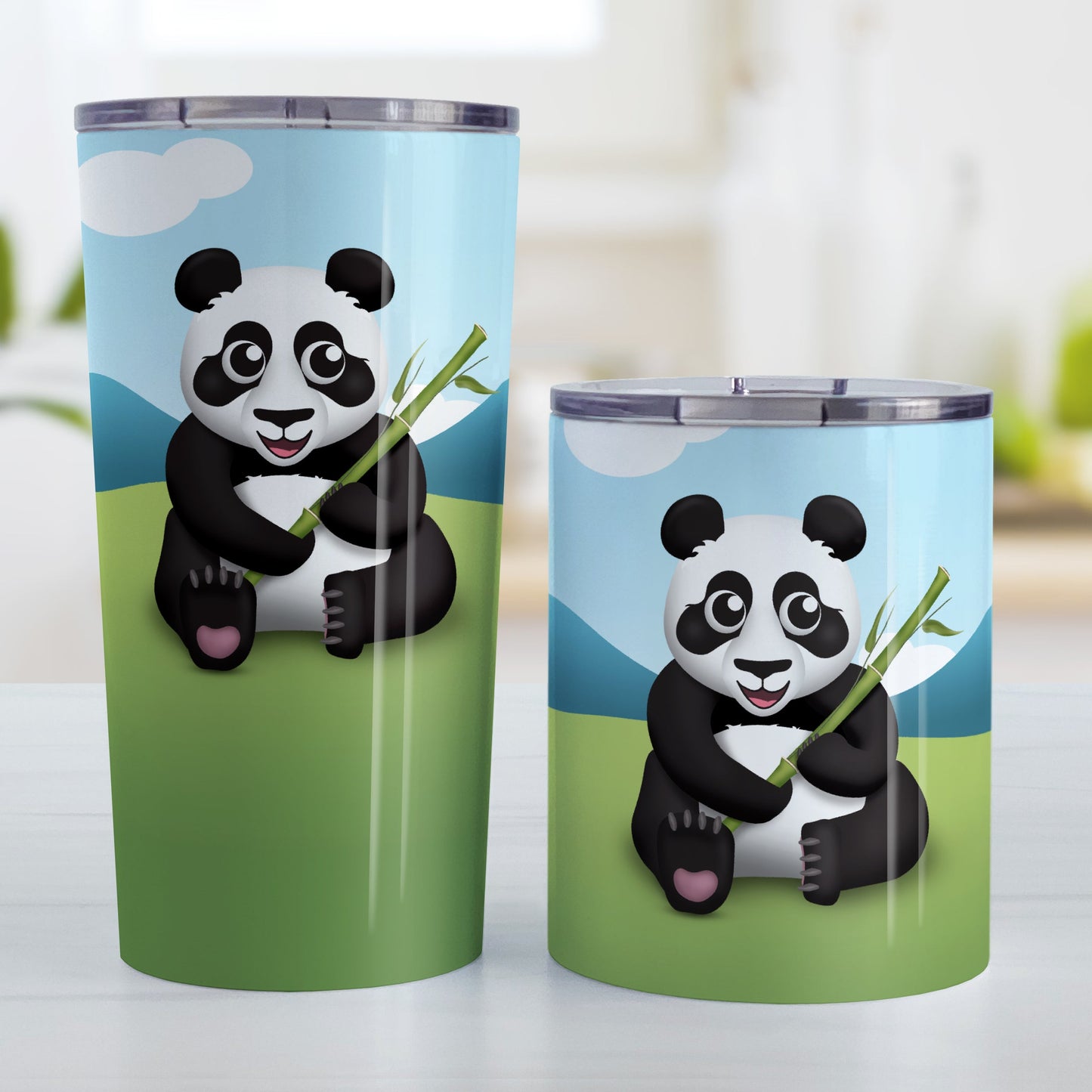 Cute Panda with Bamboo Tumbler Cup (20oz and 10oz, stainless steel insulated) at Amy's Coffee Mugs. A tumbler cup designed with an illustration of a panda holding bamboo sitting in the grass while the background illustration complete with mountains and a blue sky wraps around the cup. Photo shows both sized cups on a table next to each other.