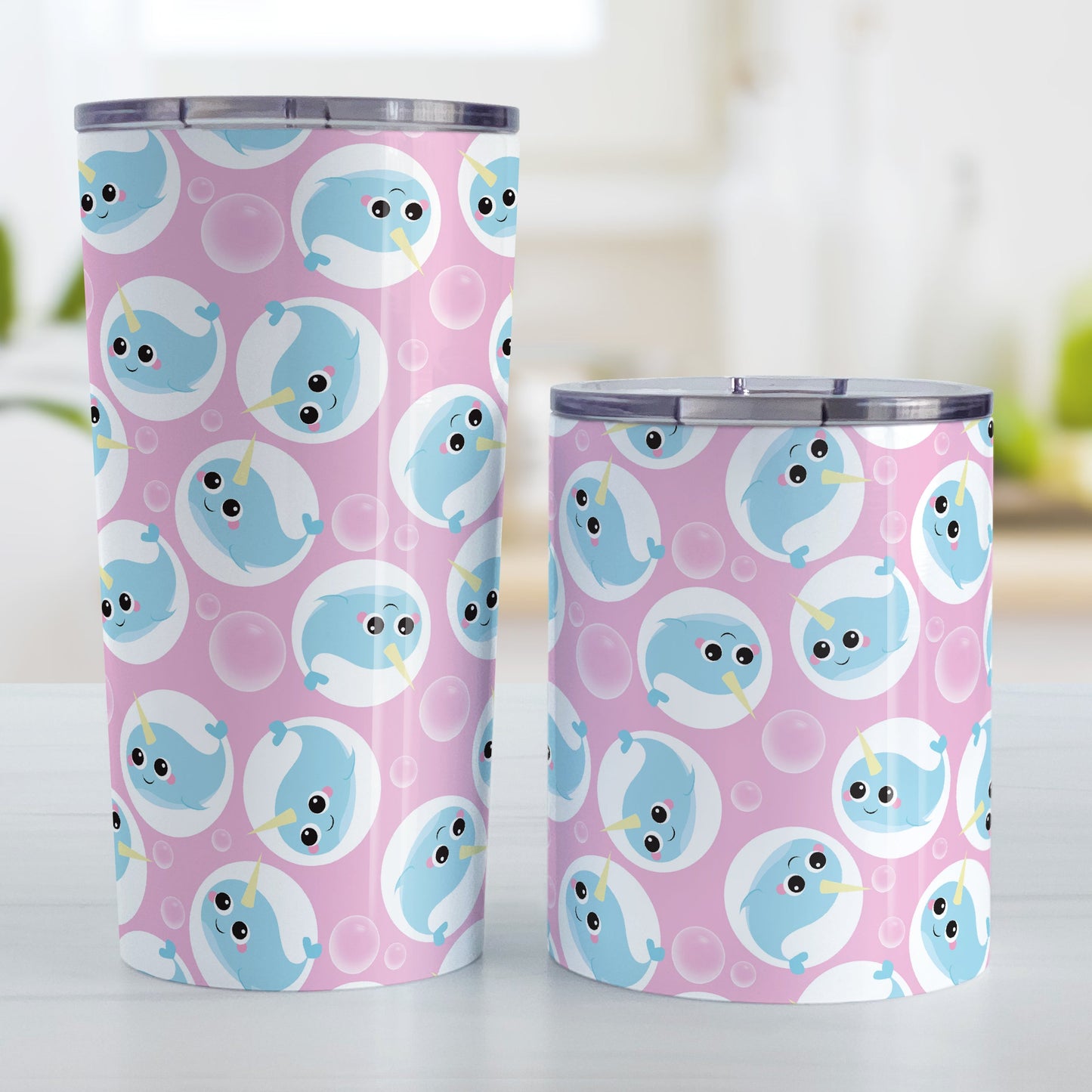 Cute Pink Narwhal Bubble Pattern Tumbler Cup (20oz and 10oz, stainless steel insulated) at Amy's Coffee Mugs. A tumbler cup designed with cute light blue narwhals in white circles and with bubbles scattered over a pink background color in a pattern that wraps around the cup. Photo shows both sized cups on a table next to each other.