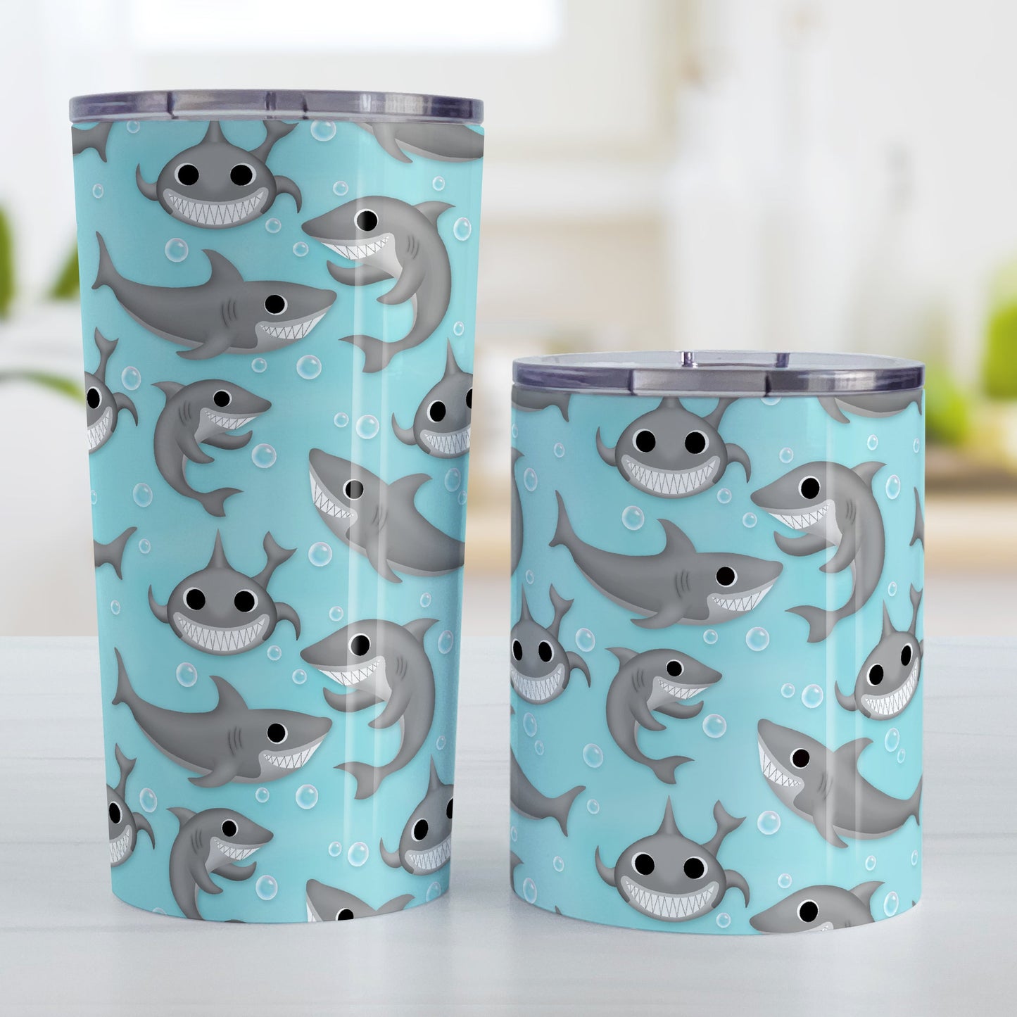 Cute Underwater Shark Pattern Tumbler Cup (20oz and 10oz, stainless steel insulated) at Amy's Coffee Mugs. Tumbler cups designed with happy and smiling sharks and bubbles in a pattern over a turquoise blue water background that wraps around the cups. Photo shows both sized cups on a table next to each other.