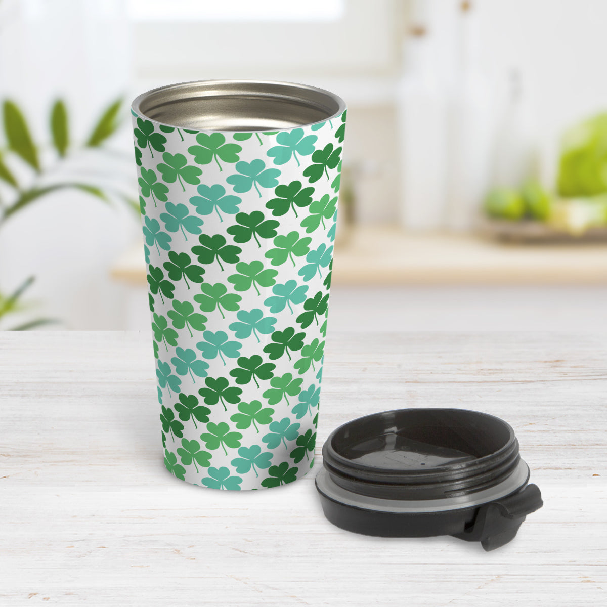 Green and Teal Clovers Travel Mug (15oz, stainless steel insulated) at Amy's Coffee Mugs. A travel mug designed with a pattern of two-tone green and teal clovers (shamrocks) that wraps around the travel mug. Photo shows the mug open on a table with the lid beside it.
