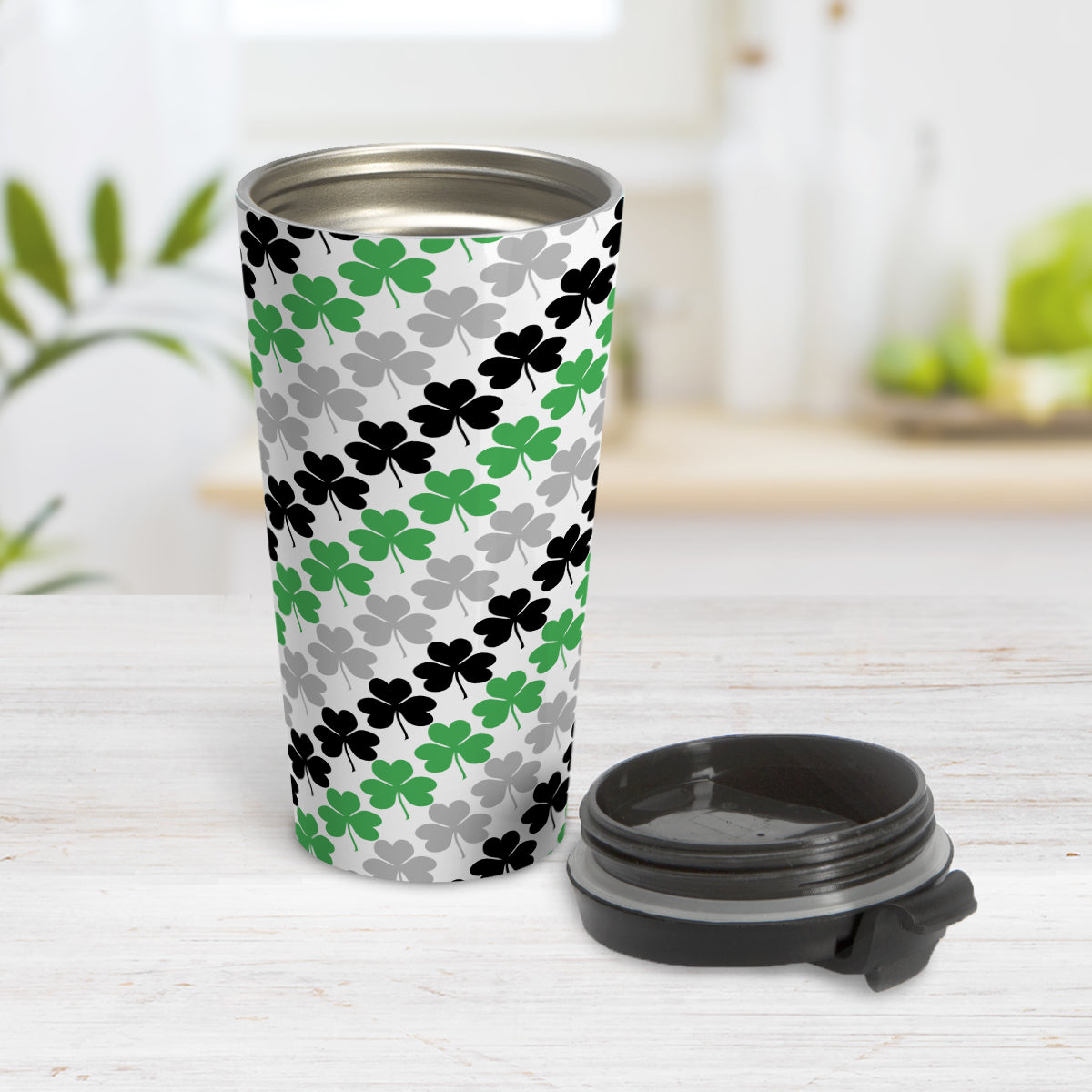 Green Black and Gray Clovers Travel Mug (15oz, stainless steel insulated) at Amy's Coffee Mugs. A travel mug designed with a pattern of green, black, and gray clovers (shamrocks) that wraps around the travel mug. Photo show the mug open on a table with its lid beside it.