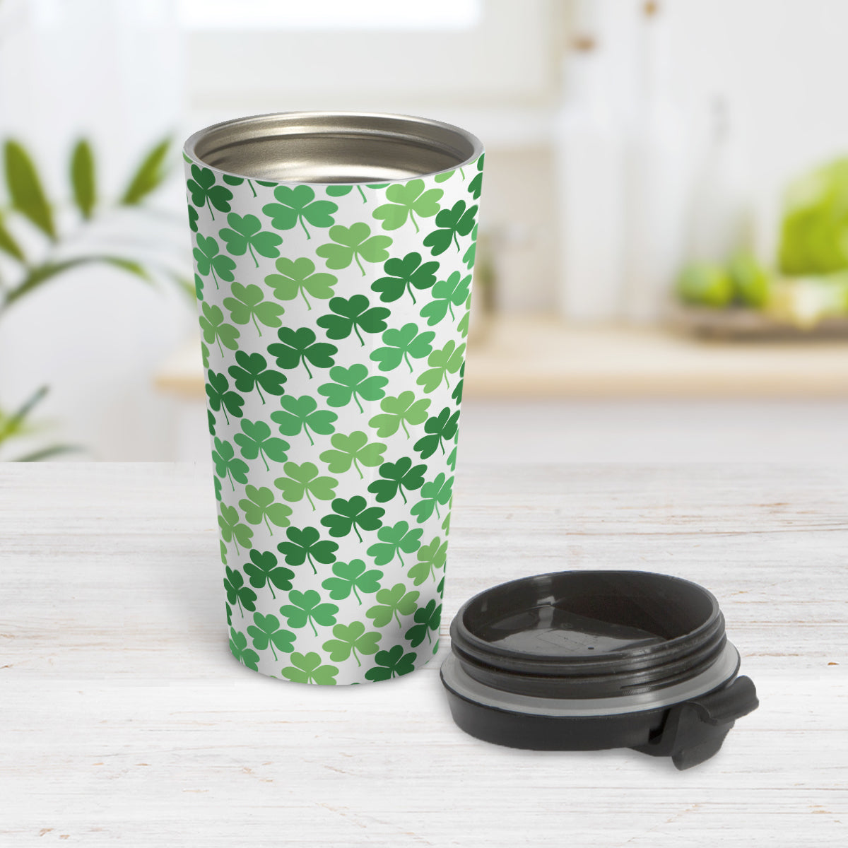 Green Clovers Travel Mug (15oz, stainless steel insulated) at Amy's Coffee Mugs. A travel mug designed with a pattern of clovers (shamrocks) in three different shades of green that wraps around the travel mug. Photo shows the mug open on a table with its lid beside it.