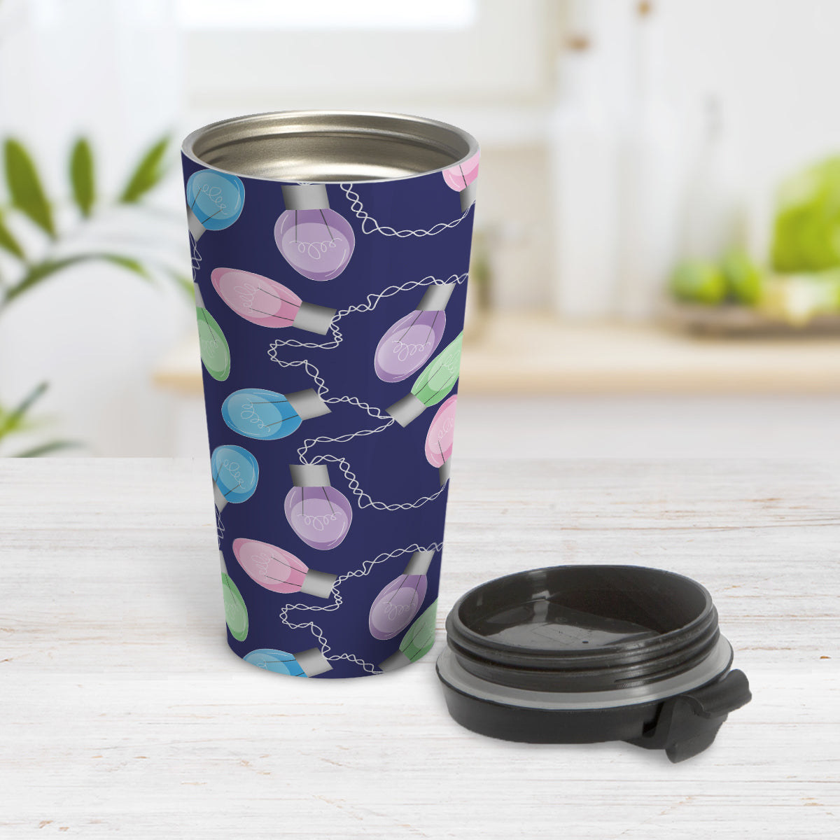 Holiday Lights Pattern Christmas Travel Mug (15oz) at Amy's Coffee Mugs. A travel mug designed with string of colorful holiday lights in pink, blue, green, and purple in a pattern over a navy blue background color that wraps around the mug up to the mug. Photo shows the mug open on a table with its lid beside it.