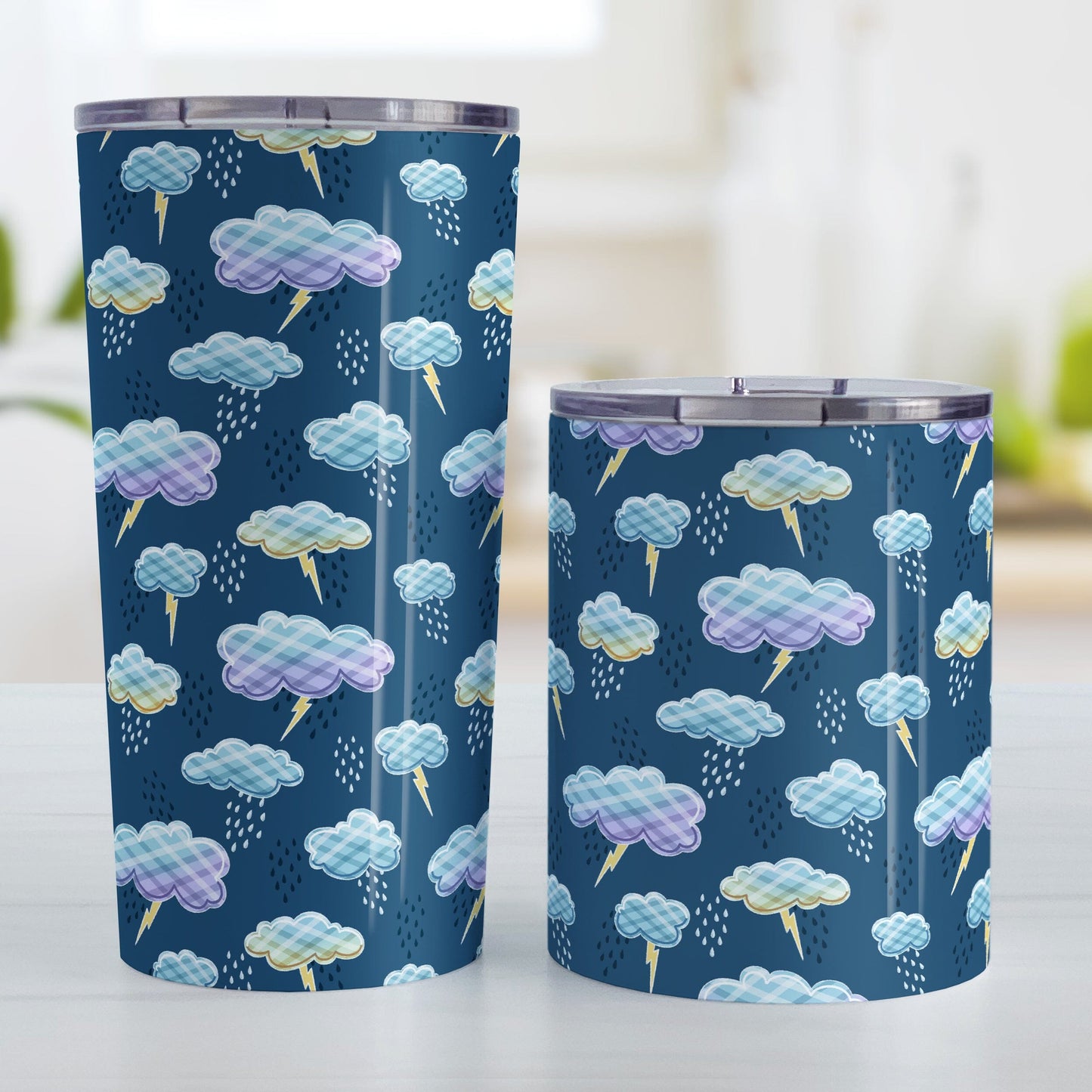 My Thunderstorm Tumbler Cups (20oz or 10oz) at Amy's Coffee Mugs. Stainless steel tumbler cups designed with an adorable thunderstorm pattern with cute illustrated storm clouds with a plaid-like pattern, lightning bolts, and rain over a dark blue background. Photo shows both sized cups on a table next to each other.