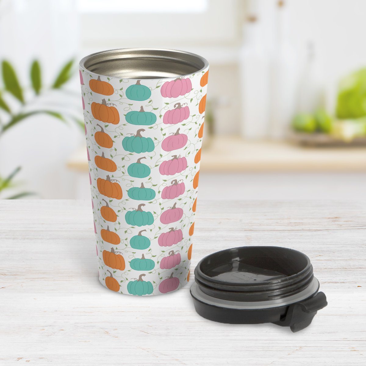 Orange Teal Pink Pumpkin Pattern Travel Mug at Amy's Coffee Mugs. A travel mug designed with a pattern of orange, teal, and pink pumpkins over a green vine and leaves pattern on a white background that wraps around the mug. Photo shows the mug open on a table with its lid beside it.