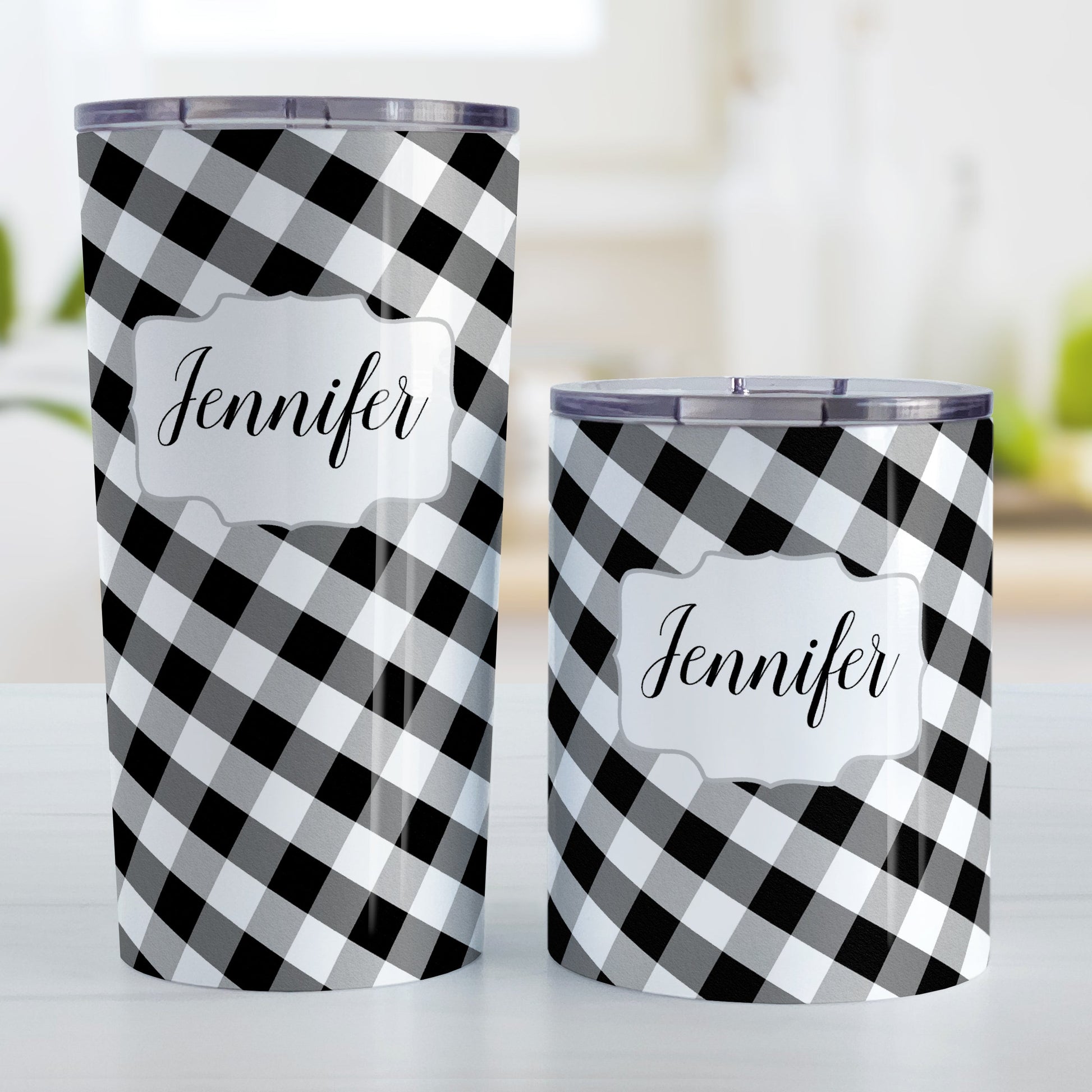 Personalized Black and White Gingham Tumbler Cup (20oz and 10oz, stainless steel insulated) at Amy's Coffee Mugs. A tumbler cup designed with a slanted black and white gingham pattern that wraps around the cup. Your name is printed in a pretty black script font in a white frame design over the gingham pattern. Photo shows both sized cups on a table next to each other.