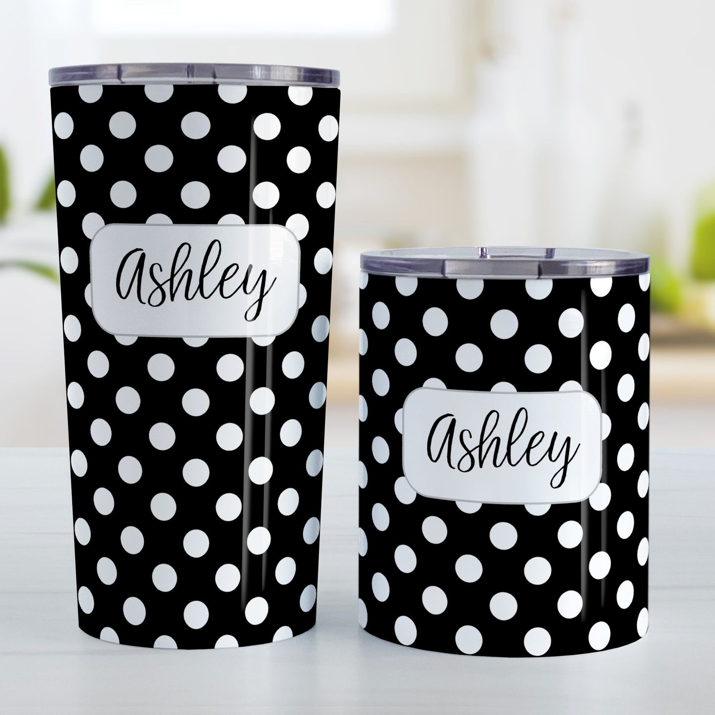 Personalized Black Polka Dot Tumbler Cup (20oz and 10oz, stainless steel insulated) at Amy's Coffee Mugs. A tumbler cup designed with a pattern of white polka dots over a black background color that wraps around the cup. Your name is personalized in a cute black script font in a white frame design over the polka dot pattern. Photo shows both sized cups on a table next to each other.