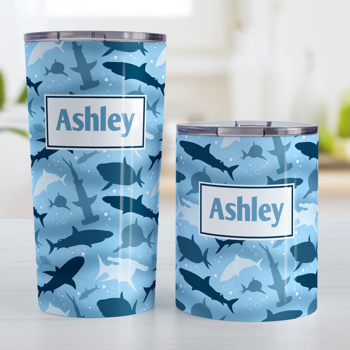 Personalized Blue Frenzy Sharks Tumbler Cups (20oz or 10oz) at Amy's Coffee Mugs. Stainless steel insulated tumbler cups designed with a pattern of sharks in different shades of blue, in a frenzy deep beneath the water, that wraps around the cups. Your personalized name is custom printed in blue over the shark pattern. Photo shows both sized cups next to each other.