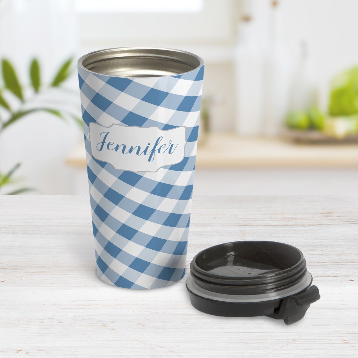 Personalized Blue Gingham Travel Mug at Amy's Coffee Mugs. A travel mug designed with a slanted blue and white gingham pattern that wraps around the travel mug. Your personalized name is custom-printed in a blue script font in a white frame design over the gingham pattern. Photo shows the mug open on a table with its lid beside it.
