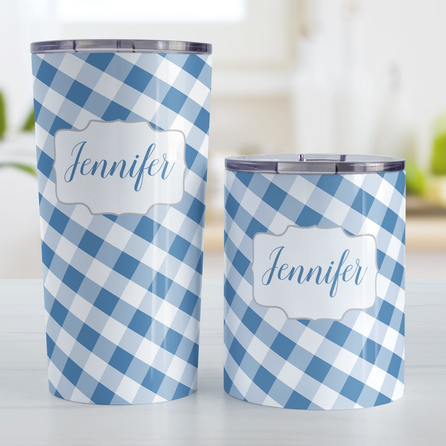 Personalized Blue Gingham Tumbler Cup (20oz and 10oz, stainless steel insulated) at Amy's Coffee Mugs. A tumbler cup designed with a slanted blue and white gingham pattern that wraps around the cup. Your personalized name is custom-printed in a blue script font in a white frame design over the gingham pattern. Photo shows both sized cups on a table next to each other.