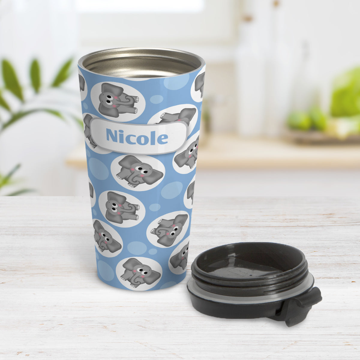 Personalized Cute Blue Elephant Pattern Travel Mug (15oz) at Amy's Coffee Mugs. A travel mug designed with cute and affectionate gray elephants in white circles scattered over a blue background color in a pattern that wraps around the travel mug. Your name is custom printed in blue on white over the elephant pattern. Photo shows the mug open on a table with its lid next to it.