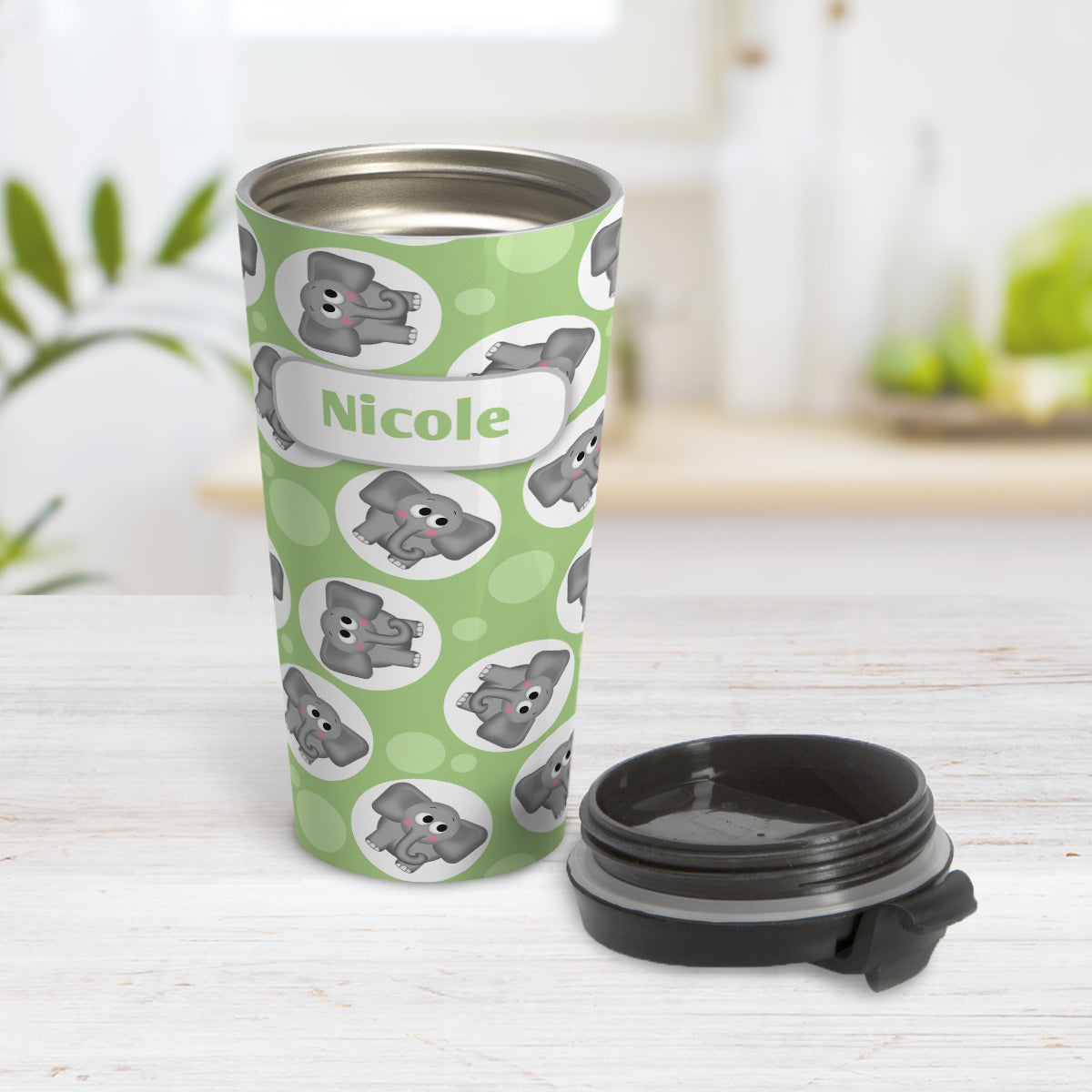 Personalized Cute Green Elephant Pattern Travel Mug (15oz) at Amy's Coffee Mugs. A travel mug designed with cute and affectionate gray elephants in white circles scattered over a green background color in a pattern that wraps around the travel mug. Your name is custom printed in green on white positioned over the elephant pattern. Photo shows the mug open on a table with its lid beside it.