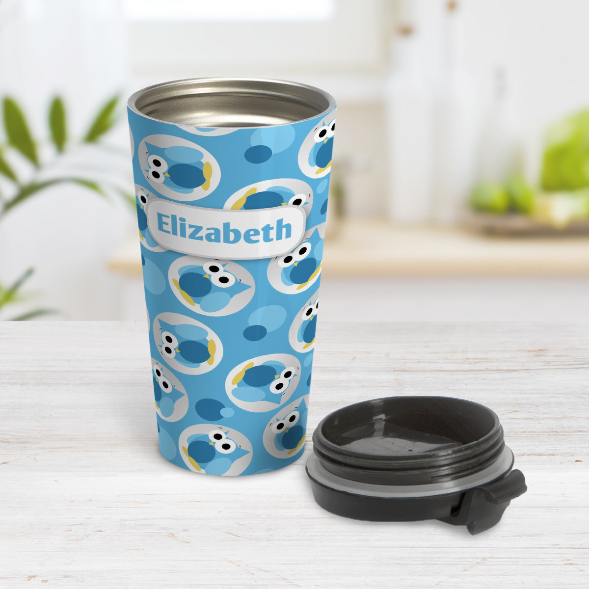 Personalized Funny Cute Blue Owl Pattern Travel Mug (15oz) at Amy's Coffee Mugs. A travel mug designed with a pattern of funny and cute blue owls in a light gray circles scattered over a blue background color that wraps around the travel mug. Your name is printed in blue in a white rectangular frame design over the owl pattern. Photo shows the mug open on a table with its lid beside it.