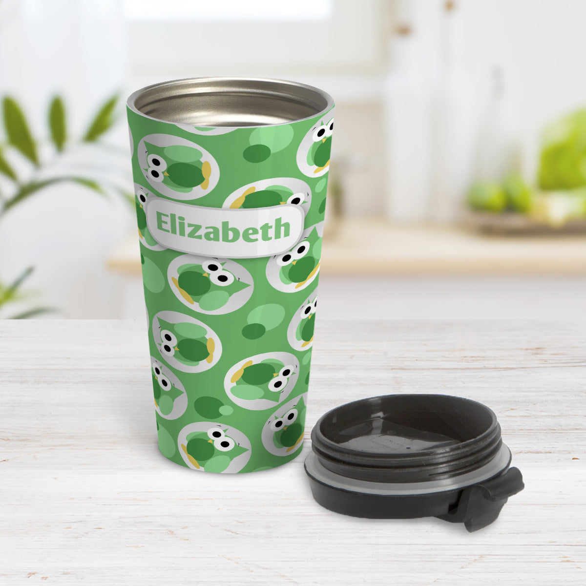 Personalized Funny Cute Green Owl Pattern Travel Mug (15oz) at Amy's Coffee Mugs. A travel mug designed with a pattern of funny and cute green owls in a light gray circles scattered over a green background color that wraps around the travel mug. Your name is printed in green in a white rectangular frame design over owl pattern. Photo shows the mug open on a table with its lid beside it.