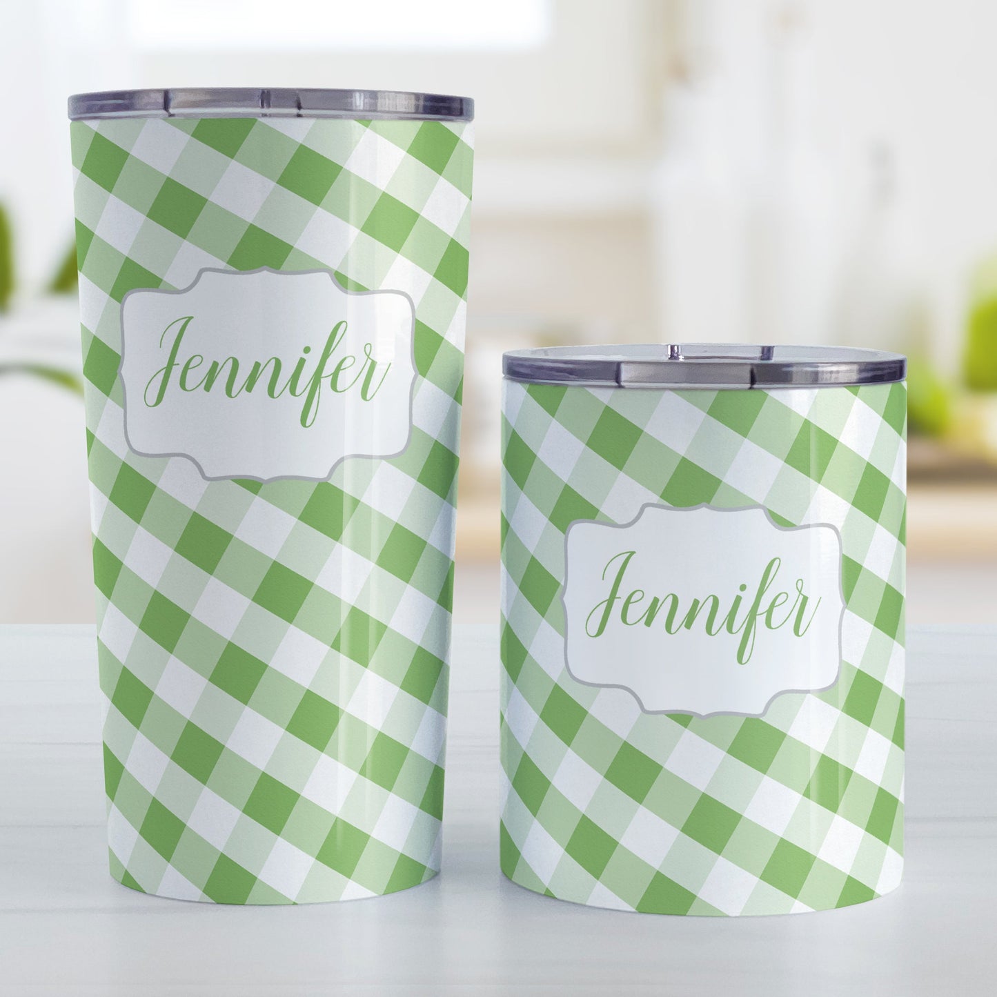 Personalized Green Gingham Tumbler Cup (20oz and 10oz, stainless steel insulated) at Amy's Coffee Mugs. A tumbler cup designed with a slanted green and white gingham pattern that wraps around the cup. Your personalized name is custom-printed in a green script font in a white frame design over the gingham pattern. Photo shows both sized cups on a table next to each other.