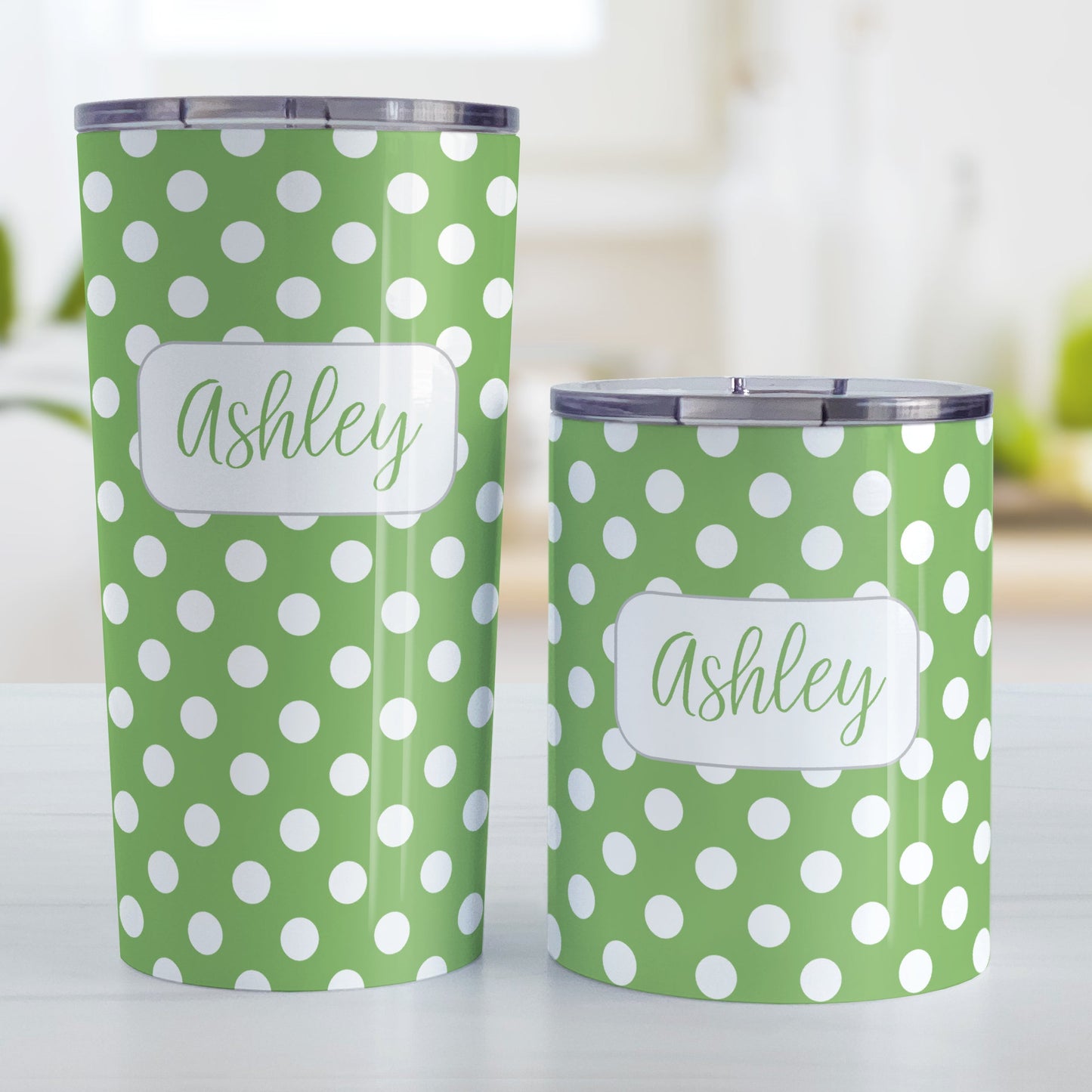 Personalized Green Polka Dot Tumbler Cup (20oz and 10oz, stainless steel insulated) at Amy's Coffee Mugs. A tumbler cup designed with a pattern of white polka dots over a green background color that wraps around the cup. Your name is personalized in a cute green script font in a white frame design over the polka dot pattern. Photo shows both sized cups on a table next to each other.