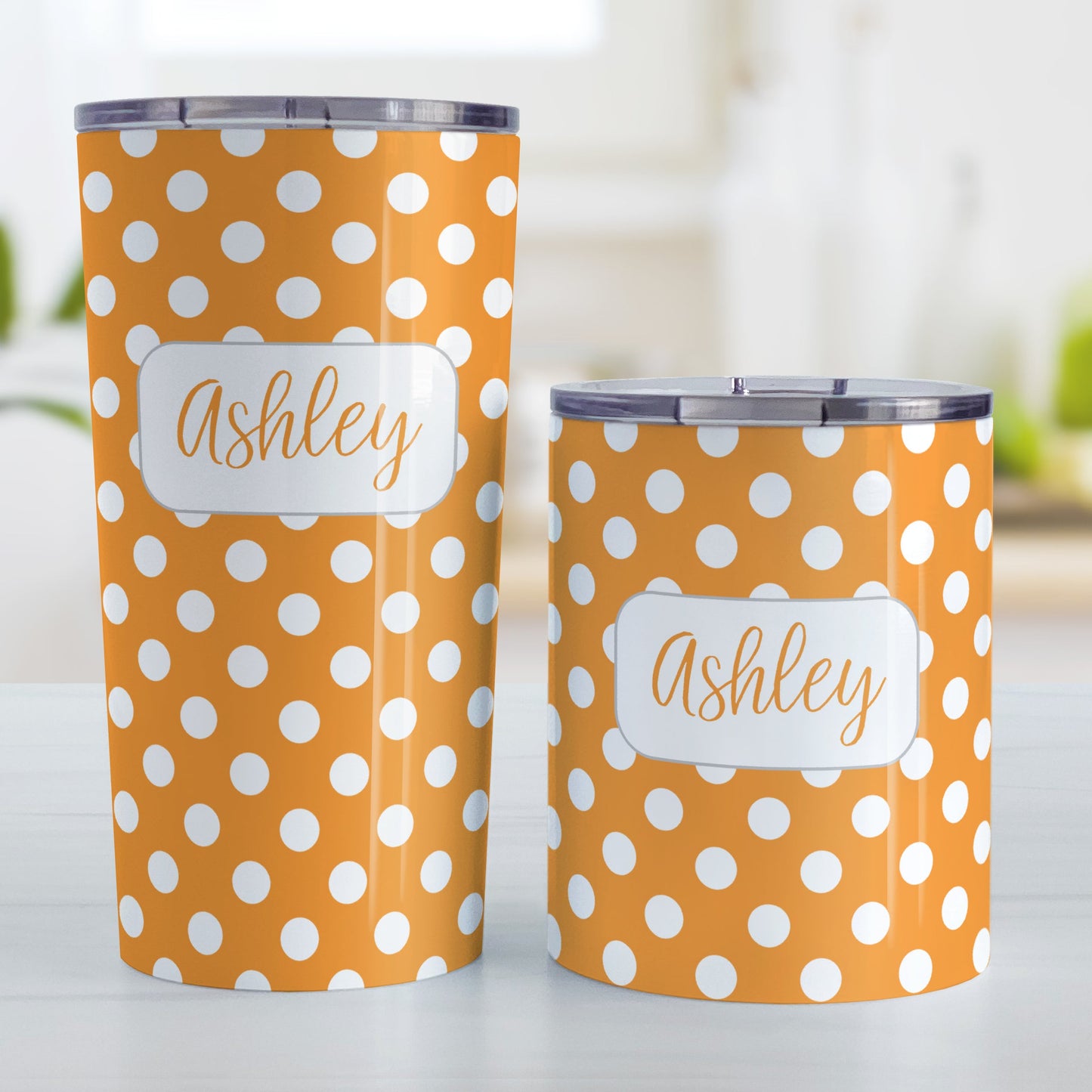 Personalized Orange Polka Dot Tumbler Cup (20oz and 10oz, stainless steel insulated) at Amy's Coffee Mugs. A tumbler cup designed with a pattern of white polka dots over an orange background color that wraps around the cup. Your name is personalized in a cute orange script font in a white frame design over the polka dot pattern. Photo shows both sized cups on a table next to each other.