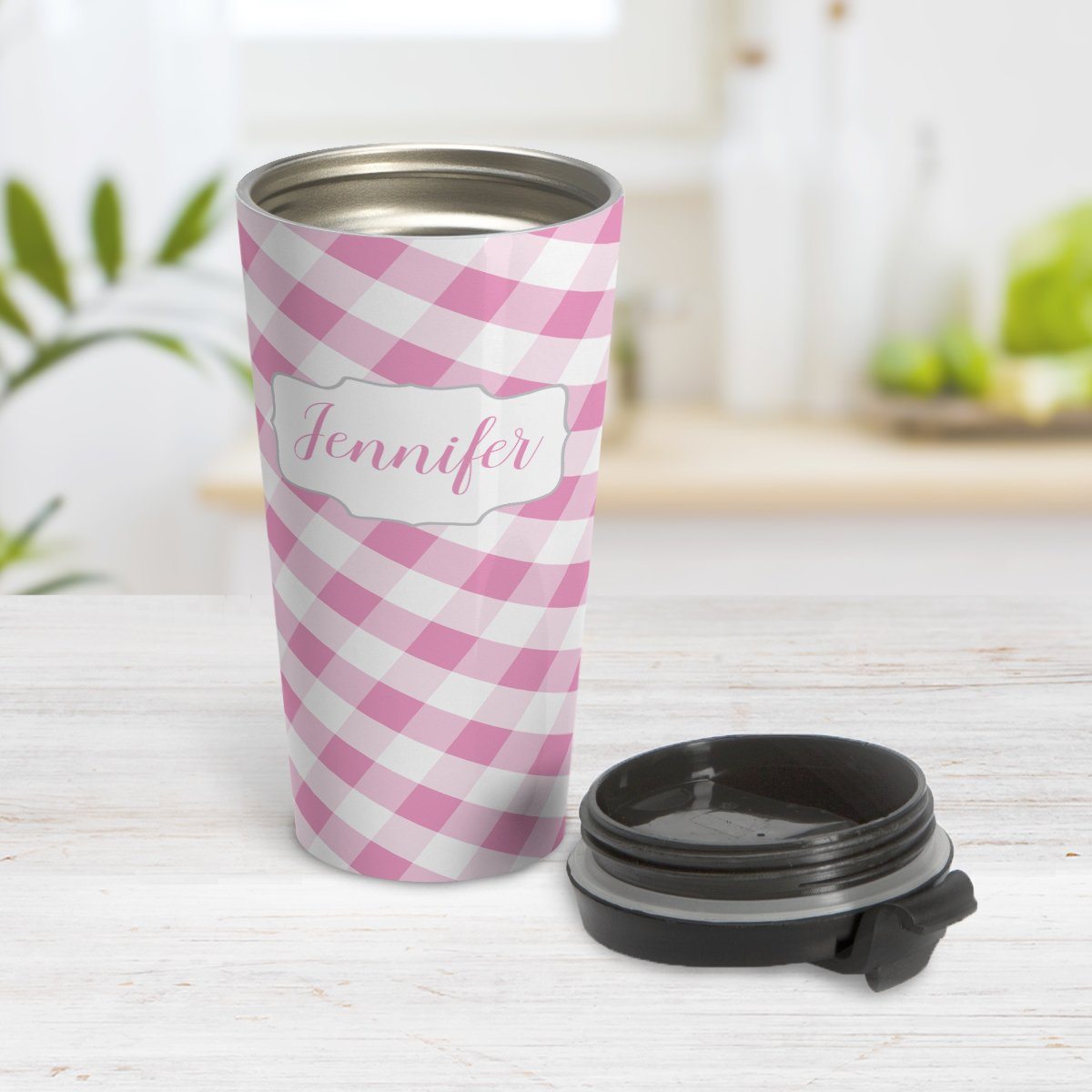 Personalized Pink Gingham Travel Mug at Amy's Coffee Mugs. A travel mug designed with a slanted pink and white gingham pattern that wraps around the travel mug. Your personalized name is custom-printed in a pink script font in a white frame design over the gingham pattern. Photo shows the mug open on a table with its lid beside it.