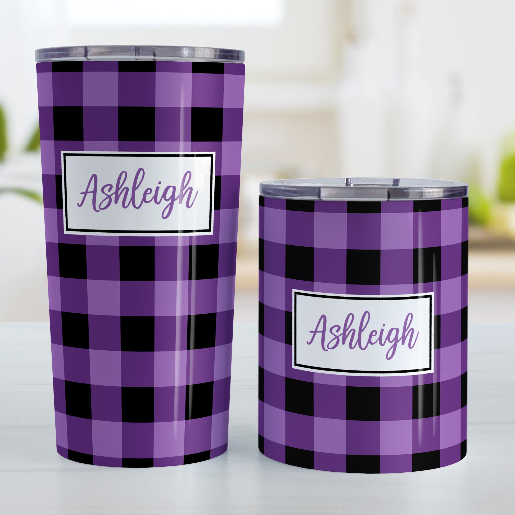 Personalized Purple and Black Buffalo Plaid Tumbler Cup (20oz and 10oz, stainless steel insulated) at Amy's Coffee Mugs. A tumbler cup designed with a purple and black buffalo plaid (buffalo check) pattern that wraps around the cup. Your name is printed in a purple script font in a white frame design over the buffalo plaid background. Photo shows both sized cups on a table next to each other.