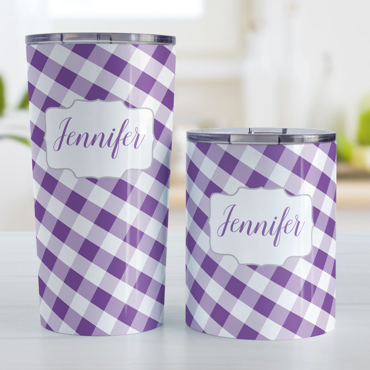 Personalized Purple Gingham Tumbler Cup (20oz and 10oz, stainless steel insulated) at Amy's Coffee Mugs. A tumbler cup designed with a slanted purple and white gingham pattern that wraps around the cup. Your personalized name is custom-printed in a purple script font in a white frame design over the gingham pattern. Photo shows both sized cups on a table next to each other.