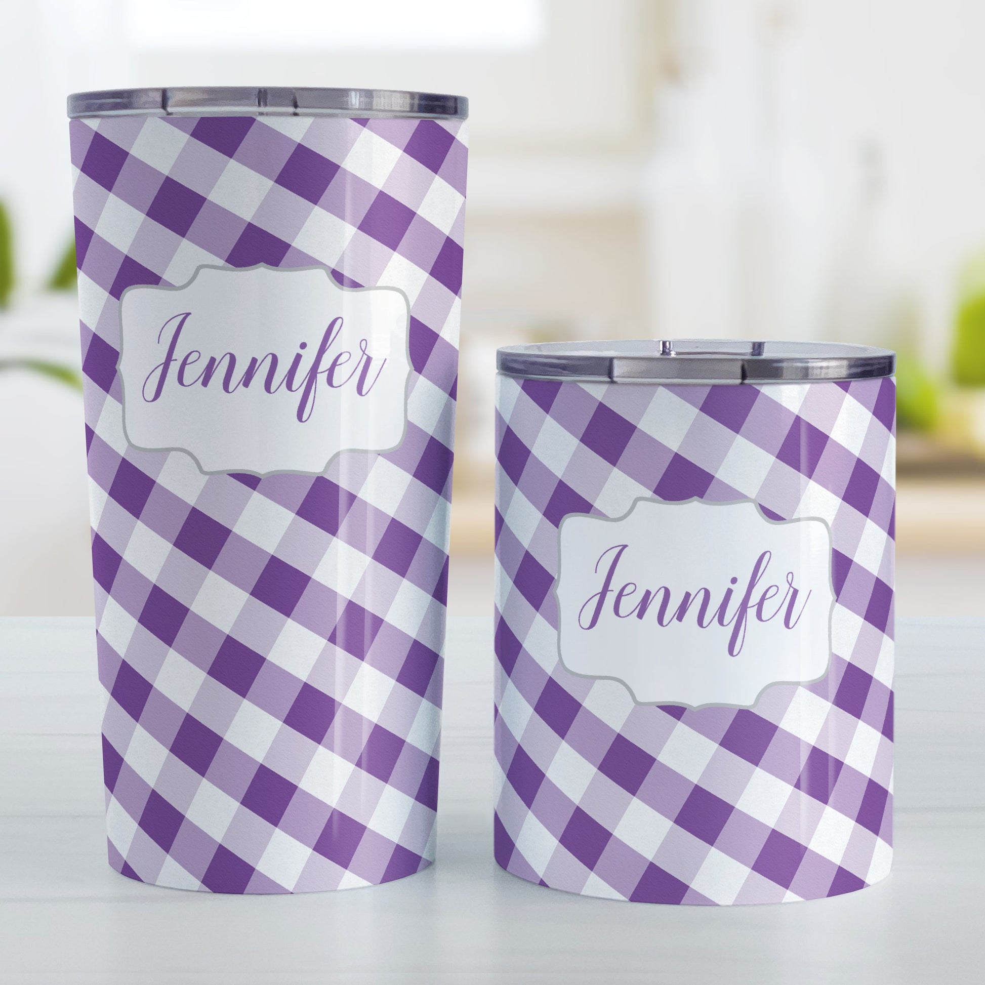Personalized Purple Gingham Tumbler Cup (20oz and 10oz, stainless steel insulated) at Amy's Coffee Mugs. A tumbler cup designed with a slanted purple and white gingham pattern that wraps around the cup. Your personalized name is custom-printed in a purple script font in a white frame design over the gingham pattern. Photo shows both sized cups on a table next to each other.