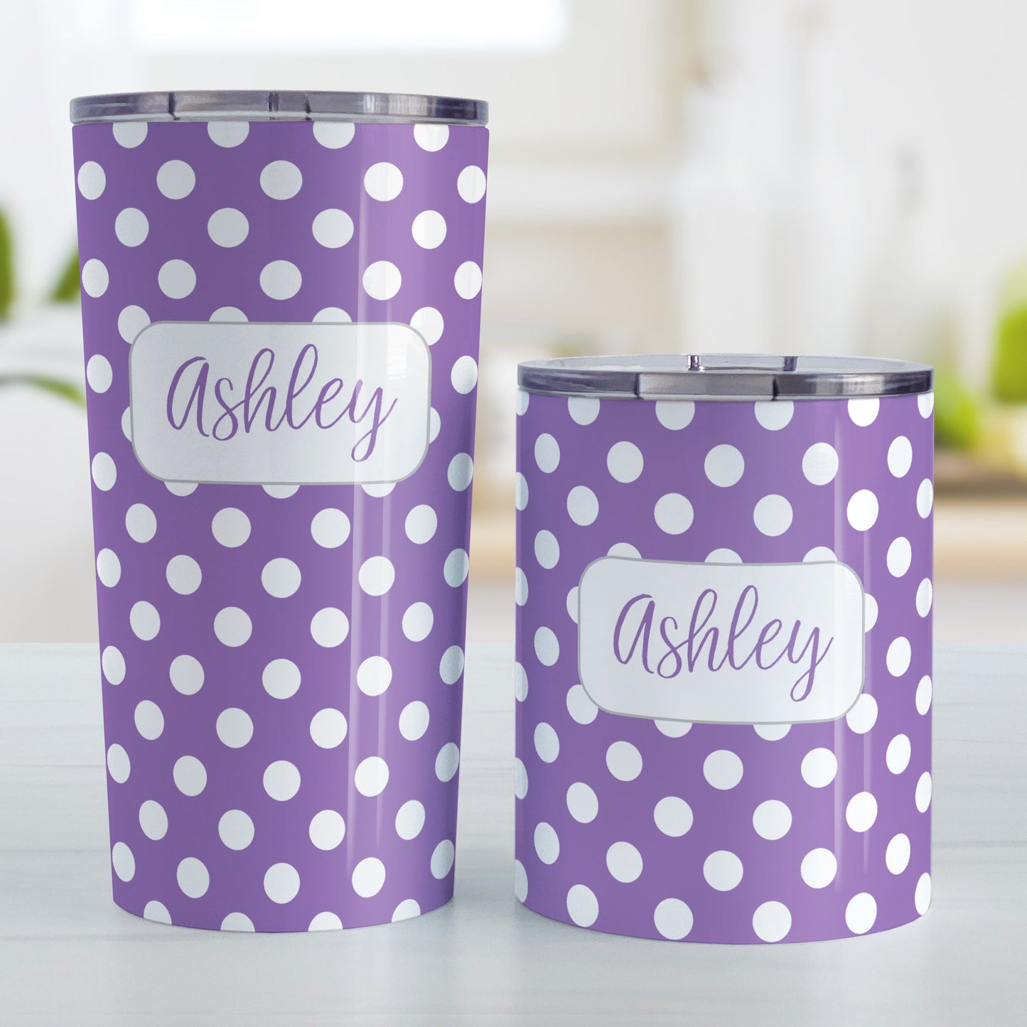 Personalized Purple Polka Dot Tumbler Cup (20oz and 10oz, stainless steel insulated) at Amy's Coffee Mugs. A tumbler cup designed with a pattern of white polka dots over a purple background color that wraps around the cup. Your name is personalized in a cute purple script font in a white frame design over the polka dot pattern. Photo shows both sized cups on a table next to each other.