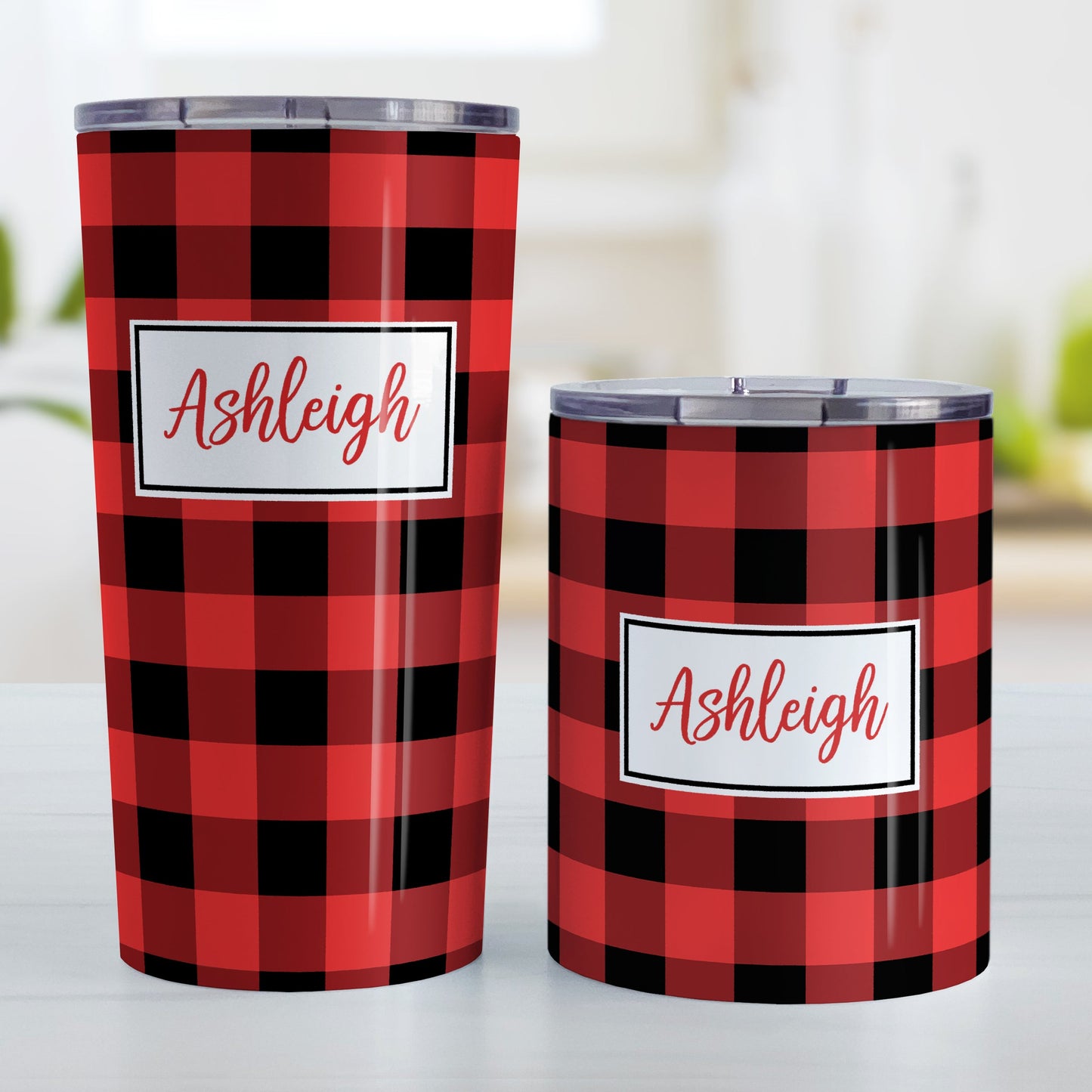 Personalized Red and Black Buffalo Plaid Tumbler Cup (20oz and 10oz, stainless steel insulated) at Amy's Coffee Mugs. A tumbler cup designed with a red and black buffalo plaid (buffalo check) pattern that wraps around the cup. Your name is printed in a red script font in a white frame design over the buffalo plaid background. Photo shows both sized cups on a table next to each other.