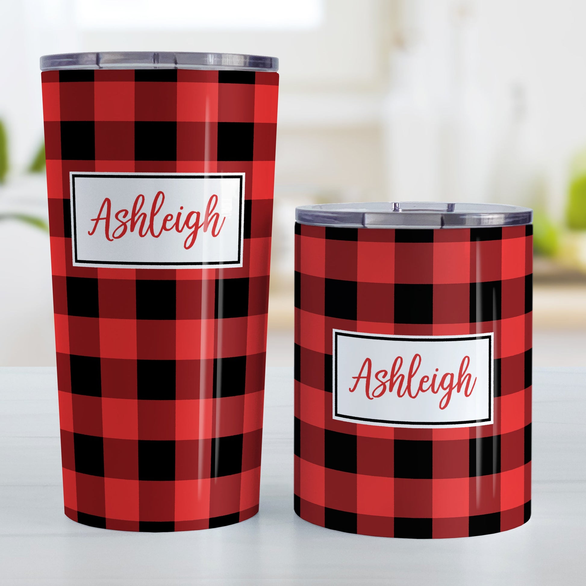 Personalized Red and Black Buffalo Plaid Tumbler Cup (20oz and 10oz, stainless steel insulated) at Amy's Coffee Mugs. A tumbler cup designed with a red and black buffalo plaid (buffalo check) pattern that wraps around the cup. Your name is printed in a red script font in a white frame design over the buffalo plaid background. Photo shows both sized cups on a table next to each other.