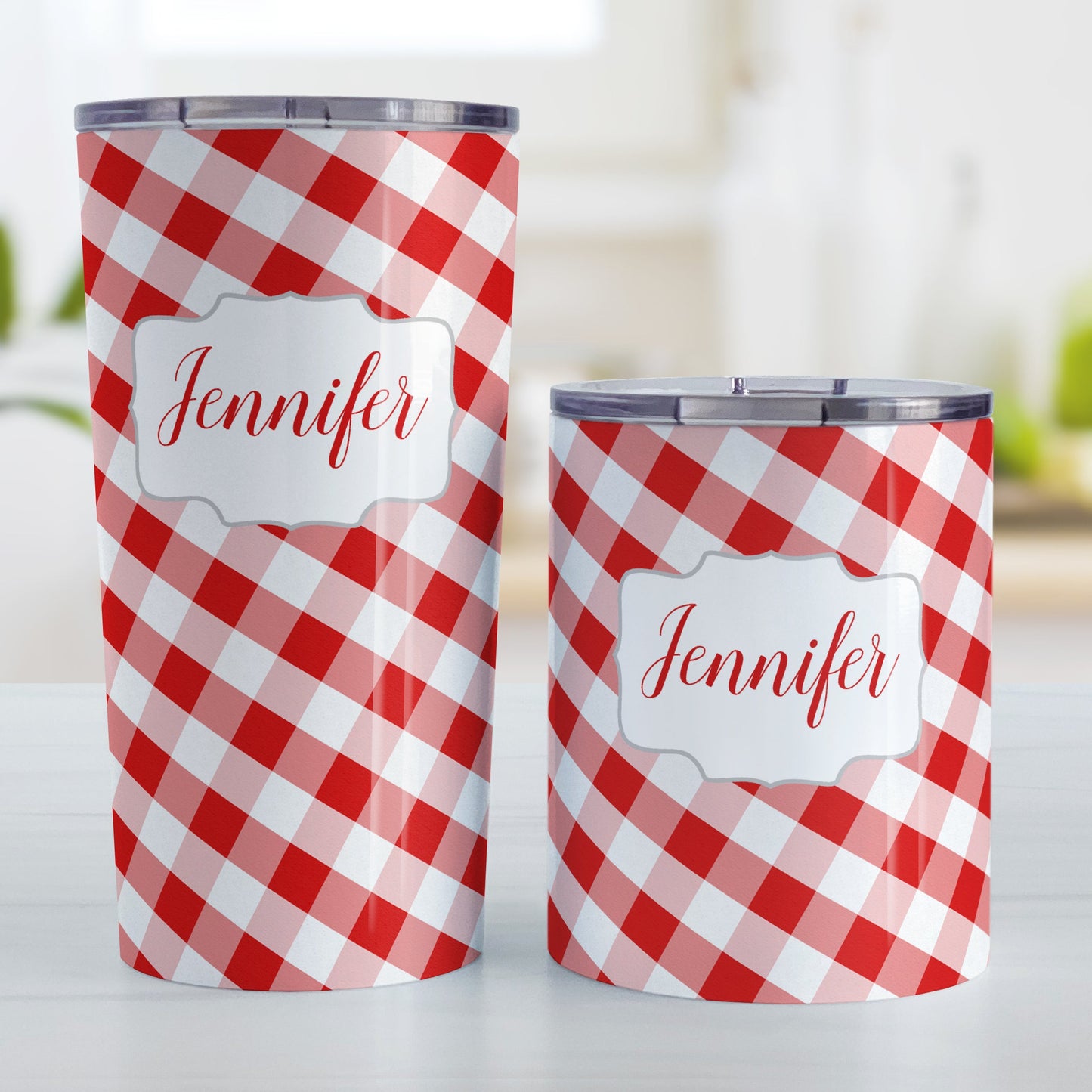 Personalized Red Gingham Tumbler Cup (20oz and 10oz, stainless steel insulated) at Amy's Coffee Mugs. A tumbler cup designed with a slanted red and white gingham pattern that wraps around the cup. Your personalized name is custom-printed in a red script font in a white frame design over the gingham pattern. Photo shows both sized cups on a table next to each other.