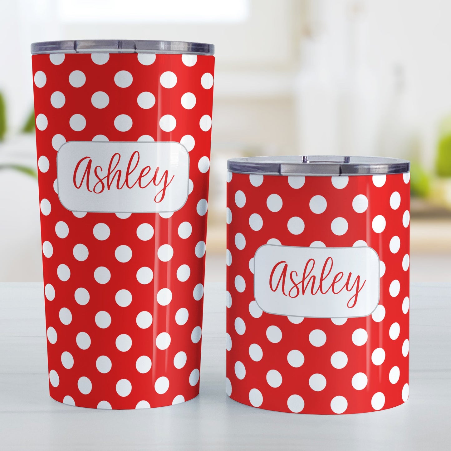 Personalized Red Polka Dot Tumbler Cup (20oz and 10oz, stainless steel insulated) at Amy's Coffee Mugs. A tumbler cup designed with a pattern of white polka dots over a red background color that wraps around the cup. Your name is personalized in a cute red script font in a white frame design over the polka dot pattern. Photo shows both sized cups on a table next to each other.
