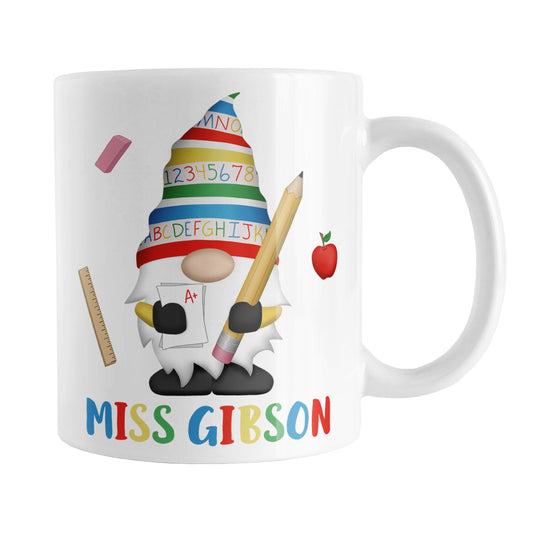Personalized School Teacher Gnome Mug (11oz) at Amy's Coffee Mugs. A ceramic coffee mug designed with an illustration of an adorable gnome wearing a festive hat with numbers and letters in primary colors and holding a large oversized pencil and graded A+ paper. Around the gnome are an eraser, a ruler, and a red apple. Your personalized name or your teacher's name is custom printed below the gnome in blue, red, yellow, and green alternating colored letters.