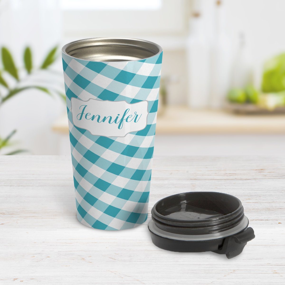 Personalized Turquoise Gingham Travel Mug at Amy's Coffee Mugs. A travel mug designed with a slanted turquoise and white gingham pattern that wraps around the travel mug. Your personalized name is custom-printed in a turquoise script font in a white frame design over the gingham pattern. Photo shows the mug open on a table with its lid beside it.