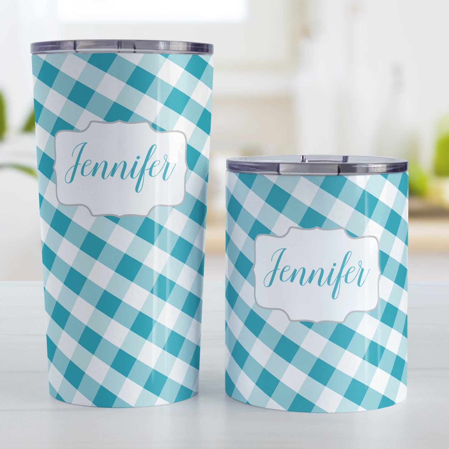Personalized Turquoise Gingham Tumbler Cup (20oz and 10oz, stainless steel insulated) at Amy's Coffee Mugs. A tumbler cup designed with a slanted turquoise and white gingham pattern that wraps around the cup. Your personalized name is custom-printed in a turquoise script font in a white frame design over the gingham pattern. Photo shows both sized cups on a table next to each other.