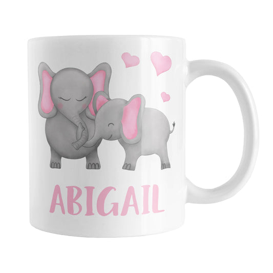 Personalized Watercolor Pink Mommy and Baby Elephants Mug (11oz) at Amy's Coffee Mugs. A ceramic coffee mug designed with affectionate pink and gray mommy and baby elephants illustrated in a watercolor design with pink hearts above them on both sides of the mug. Your personalized name is custom-printed in a cute uppercase-letters font in pink below these adorable elephants.