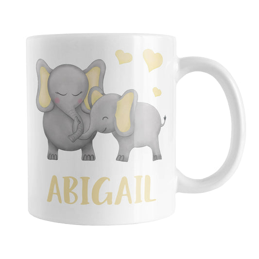 Personalized Watercolor Yellow Mommy and Baby Elephants Mug (11oz) at Amy's Coffee Mugs. A ceramic coffee mug designed with affectionate yellow and gray mommy and baby elephants illustrated in a watercolor design with yellow hearts above them on both sides of the mug. Your personalized name is custom-printed in a cute uppercase-letters font in yellow below these adorable elephants.