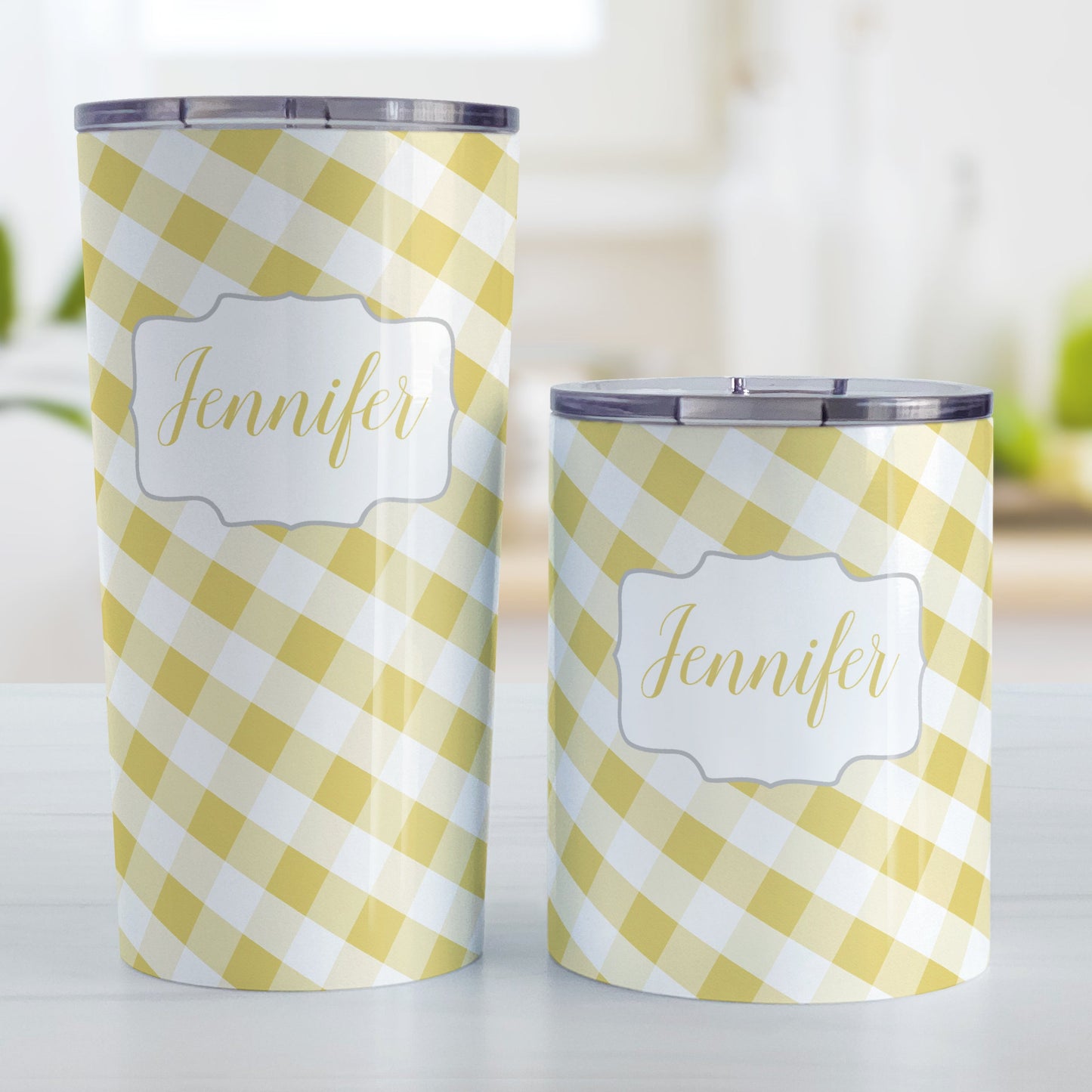 Personalized Yellow Gingham Tumbler Cup (20oz and 10oz, stainless steel insulated) at Amy's Coffee Mugs. A tumbler cup designed with a slanted yellow and white gingham pattern that wraps around the cup. Your personalized name is custom-printed in a yellow script font in a white frame design over the gingham pattern. Photo shows both sized cups on a table next to each other.