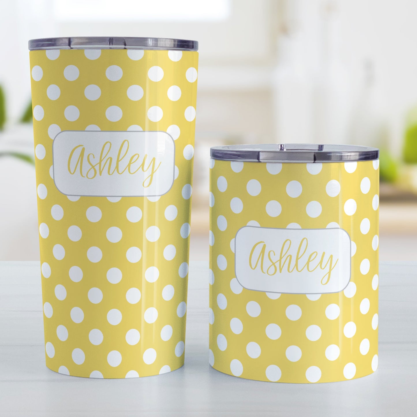 Personalized Yellow Polka Dot Tumbler Cup (20oz and 10oz, stainless steel insulated) at Amy's Coffee Mugs. A tumbler cup designed with a pattern of white polka dots over a yellow background color that wraps around the cup. Your name is personalized in a cute yellow script font in a white frame design over the polka dot pattern. Photo shows both sized cups on a table next to each other.