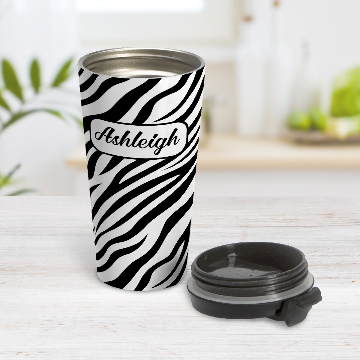 Personalized Zebra Print Pattern Travel Mug at Amy's Coffee Mugs. A travel mug designed with an animal print pattern of black and white zebra stripes that wraps around the travel mug. Your name is custom-printed in a stylish black script font in a white rectangular design over the zebra print pattern. Photo shows the mug open on a table with its lid beside it.