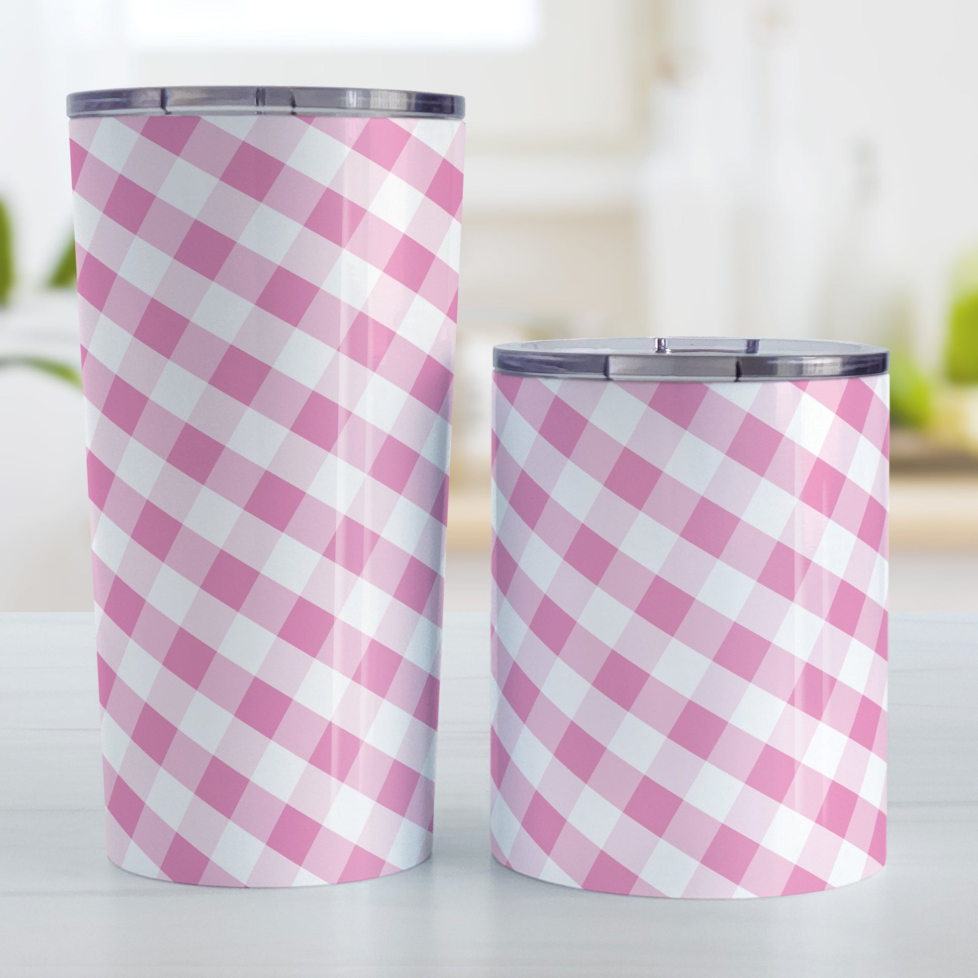Pink Gingham Tumbler Cup (20oz and 10oz, stainless steel insulated) at Amy's Coffee Mugs. A tumbler cup designed with a slanted pink and white gingham pattern that wraps around the cup. Photo shows both sized cups on a table next to each other.
