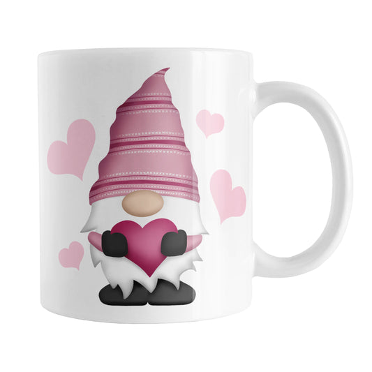 Pink Heart Gnome Mug (11oz) at Amy's Coffee Mugs. A ceramic coffee mug designed with a cute pink hat-wearing gnome holding a fuchsia pink heart with four light pink hearts around it on both sides of the mug.