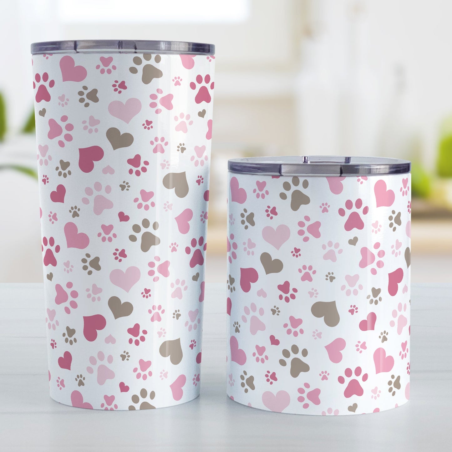 Pink Hearts and Paw Prints Tumbler Cup (20oz and 10oz) at Amy's Coffee Mugs. Stainless steel insulated tumbler cups designed with a pattern of hearts and paw prints in brown and different shades of pink that wraps around the cups. These tumbler cups are perfect for people love dogs and cute paw print designs. The photo shows both sized cups next to each other.