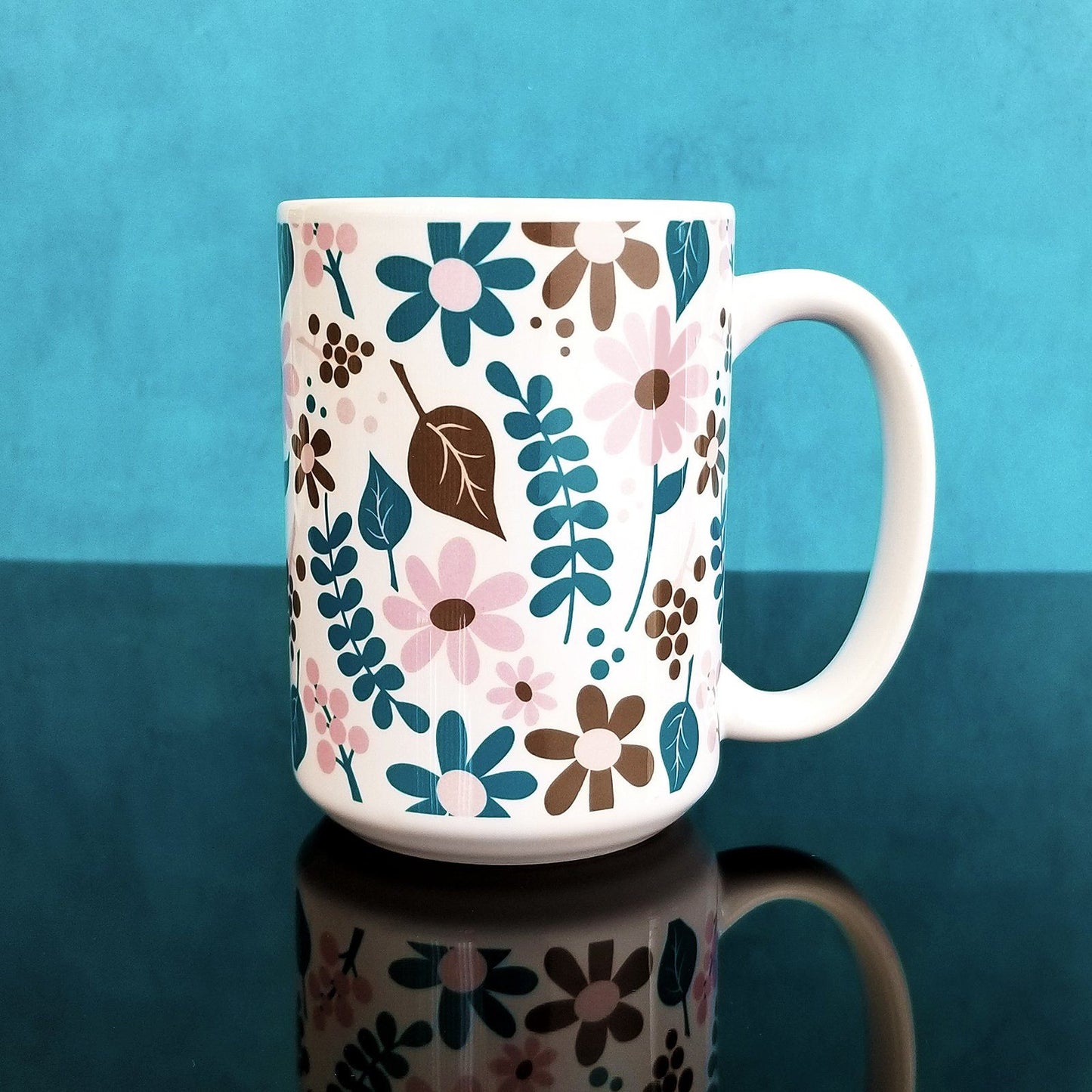 Pink Turquoise Brown Floral Pattern Mug (15oz, on blue and glossy black background) at Amy's Coffee Mugs. A ceramic coffee mug designed with a pretty flowers and leaves pattern in pink, dark turquoise, and brown that wraps around the mug up to the handle.
