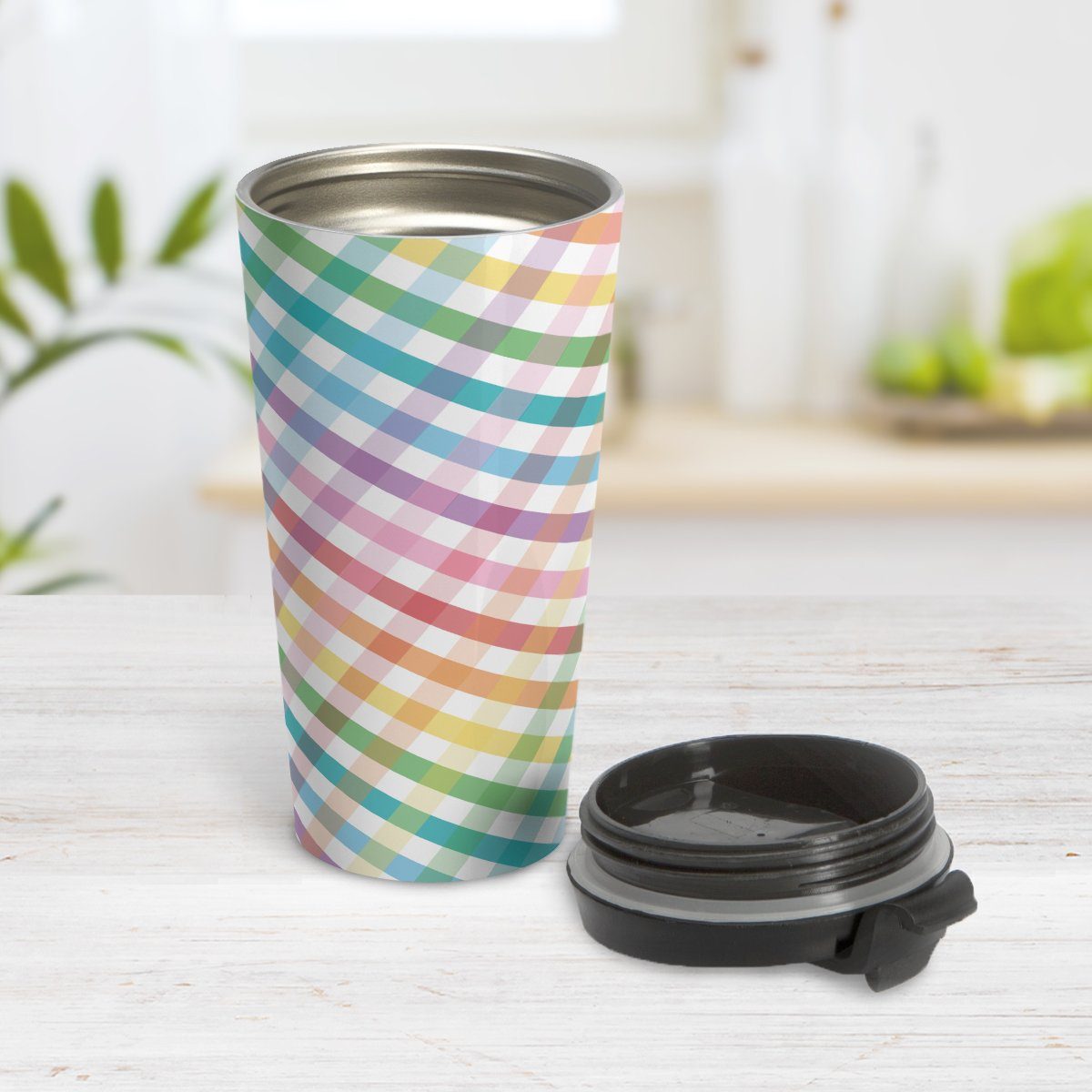 Rainbow Gingham Travel Mug at Amy's Coffee Mugs. A travel mug designed with a slanted gingham pattern with a colorful rainbow progression that wraps around the travel mug. Photo shows the mug open on a table with its lid beside it.