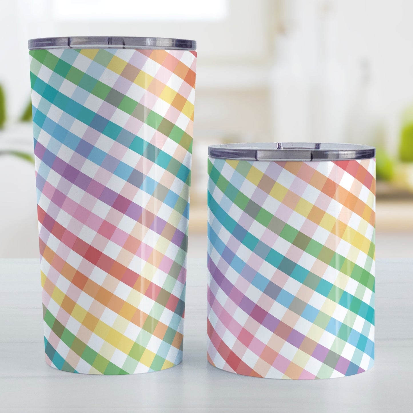 Rainbow Gingham Tumbler Cup (20oz and 10oz, stainless steel insulated) at Amy's Coffee Mugs. A tumbler cup designed with a slanted gingham pattern with a colorful rainbow progression that wraps around the cup. Photo shows both sized cups on a table next to each other.