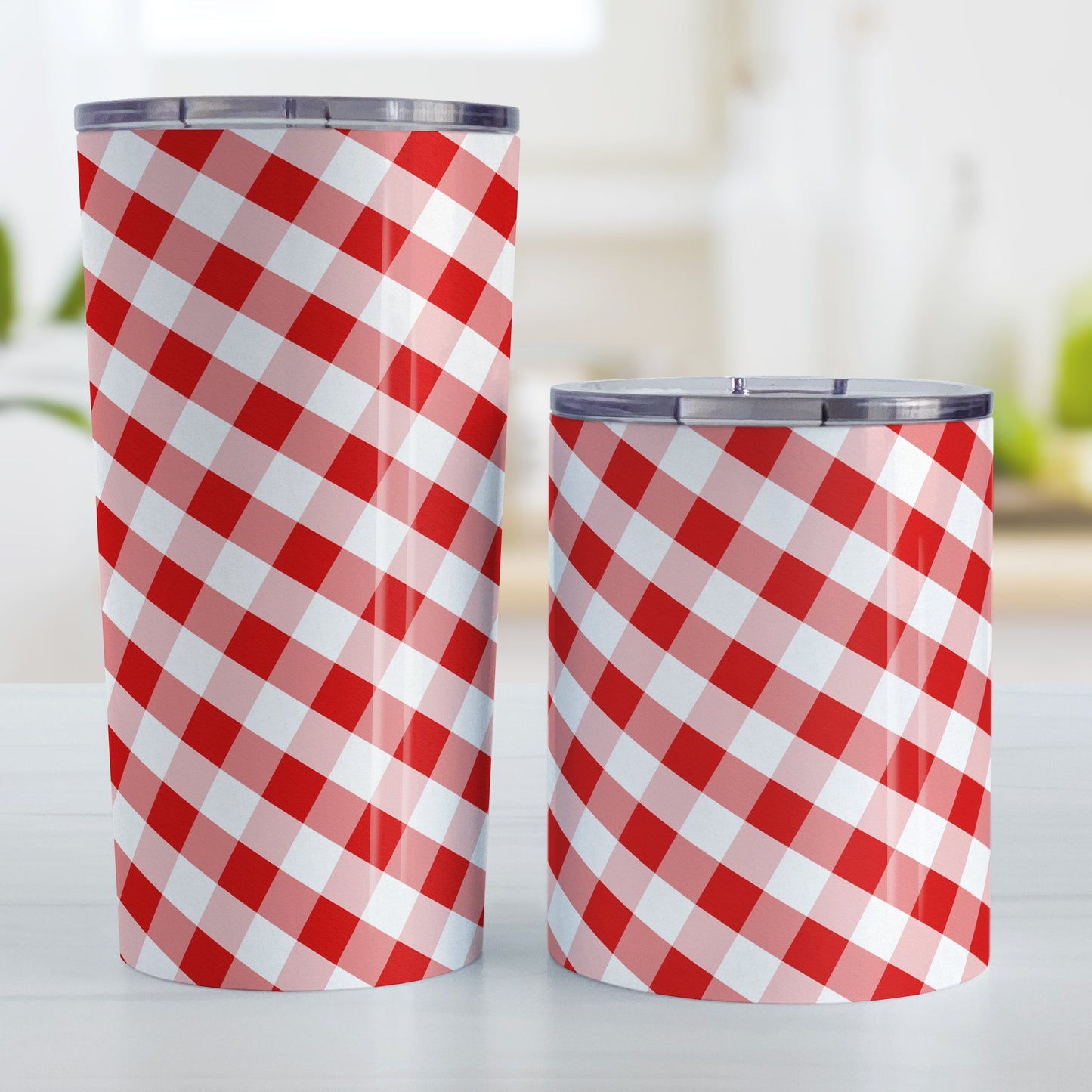 Red Gingham Tumbler Cup (20oz and 10oz, stainless steel insulated) at Amy's Coffee Mugs. A tumbler cup designed with a slanted red and white gingham pattern that wraps around the cup. Photo shows both sized cups on a table next to each other.