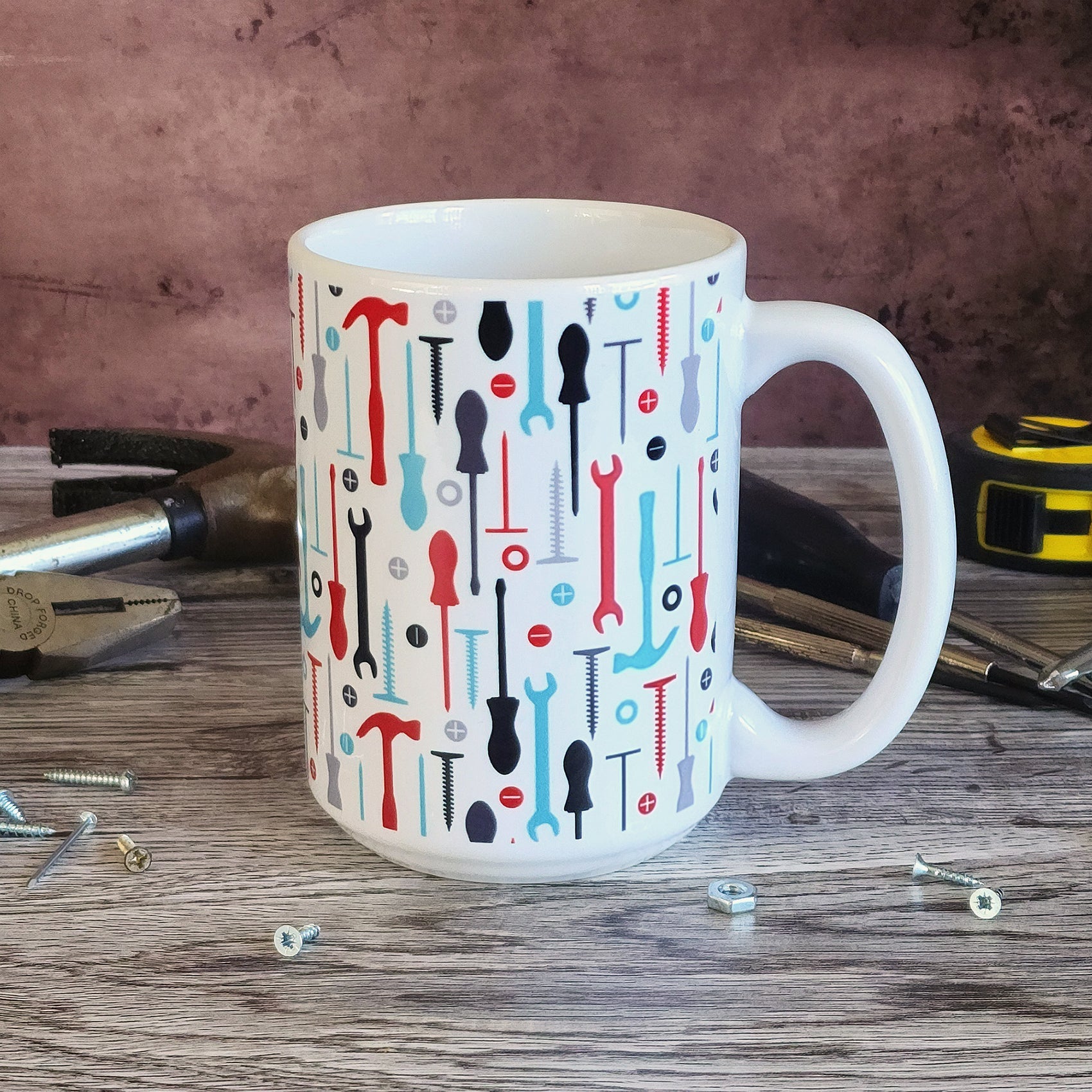 Red Turquoise Tools Pattern Mug (15oz on work bench with tools round it) at Amy's Coffee Mugs. A ceramic coffee mug with a modern style pattern of tools in red, turquoise, black, and gray over white that wraps around the mug to the handle. Perfect for any handyman or contractor.