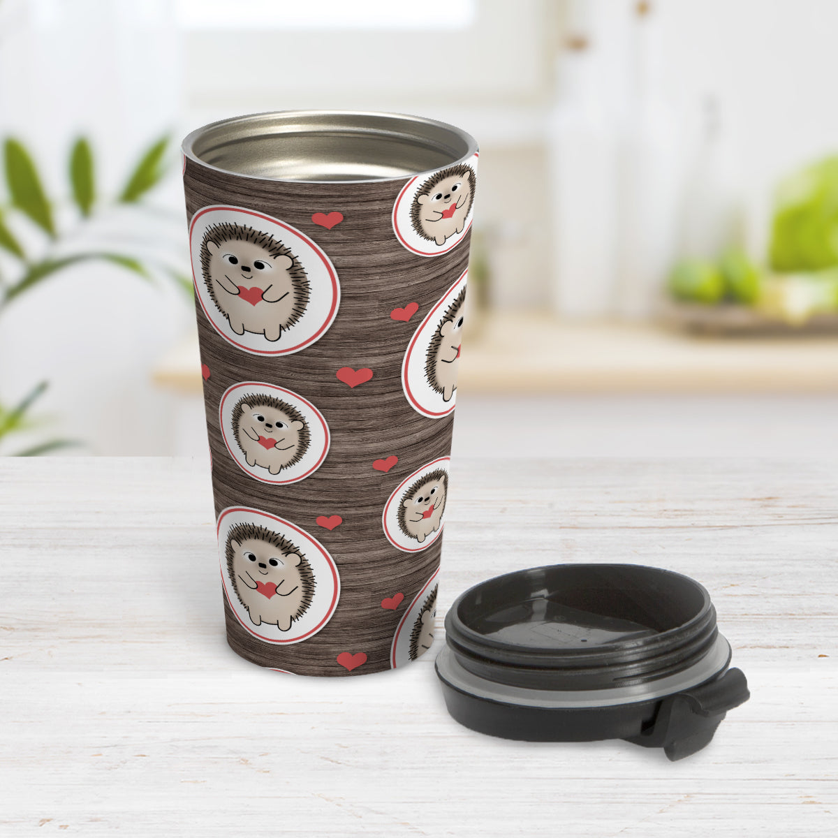 Rustic Wood Red Heart Hedgehog Travel Mug (15oz, stainless steel insulated) at Amy's Coffee Mugs. A travel mug designed with a pattern of hedgehogs holding red hearts in ovals outlined in red and scattered red hearts in a pattern over a rustic wood background design that wraps around the mug. Photo shows the mug open on a table with its lid beside it.