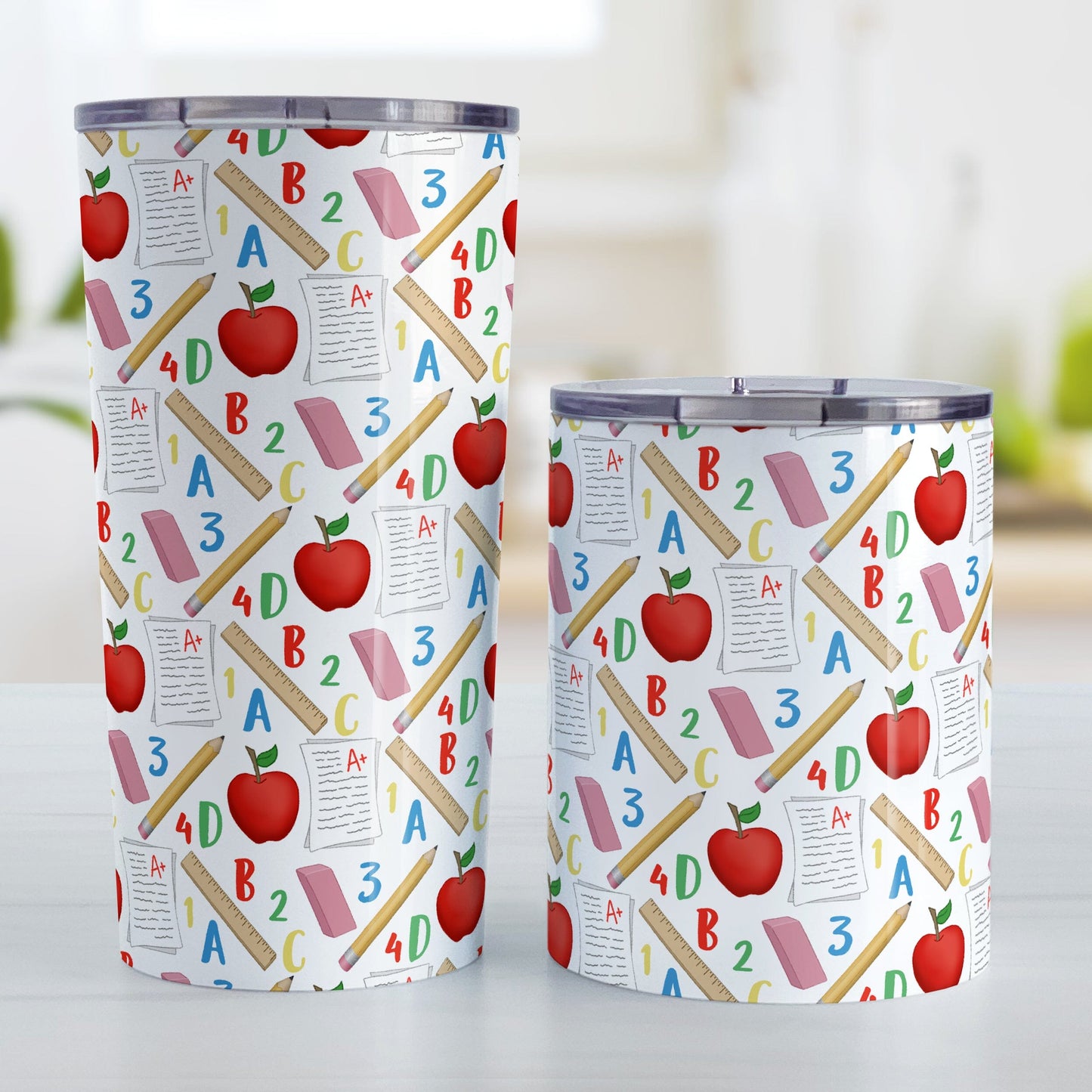 School Pattern Tumbler Cups (20oz or 10oz) at Amy's Coffee Mugs. Stainless steel tumbler cups designed with a school-themed pattern that wraps around the cups with apples, rulers, erasers, graded papers, numbers, and letters. Photo shows both sized cups on a table next to each other.