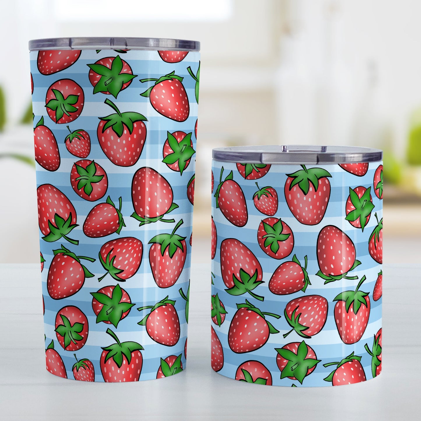 Strawberries on Blue Stripes Tumbler Cup (20oz and 10oz, stainless steel insulated) at Amy's Coffee Mugs. A tumbler cup featuring a print of hand-drawn strawberries in red and green in an assorted pattern over a blue stripes background that wraps around the cup. Photo shows both sized cups on a table next to each other.